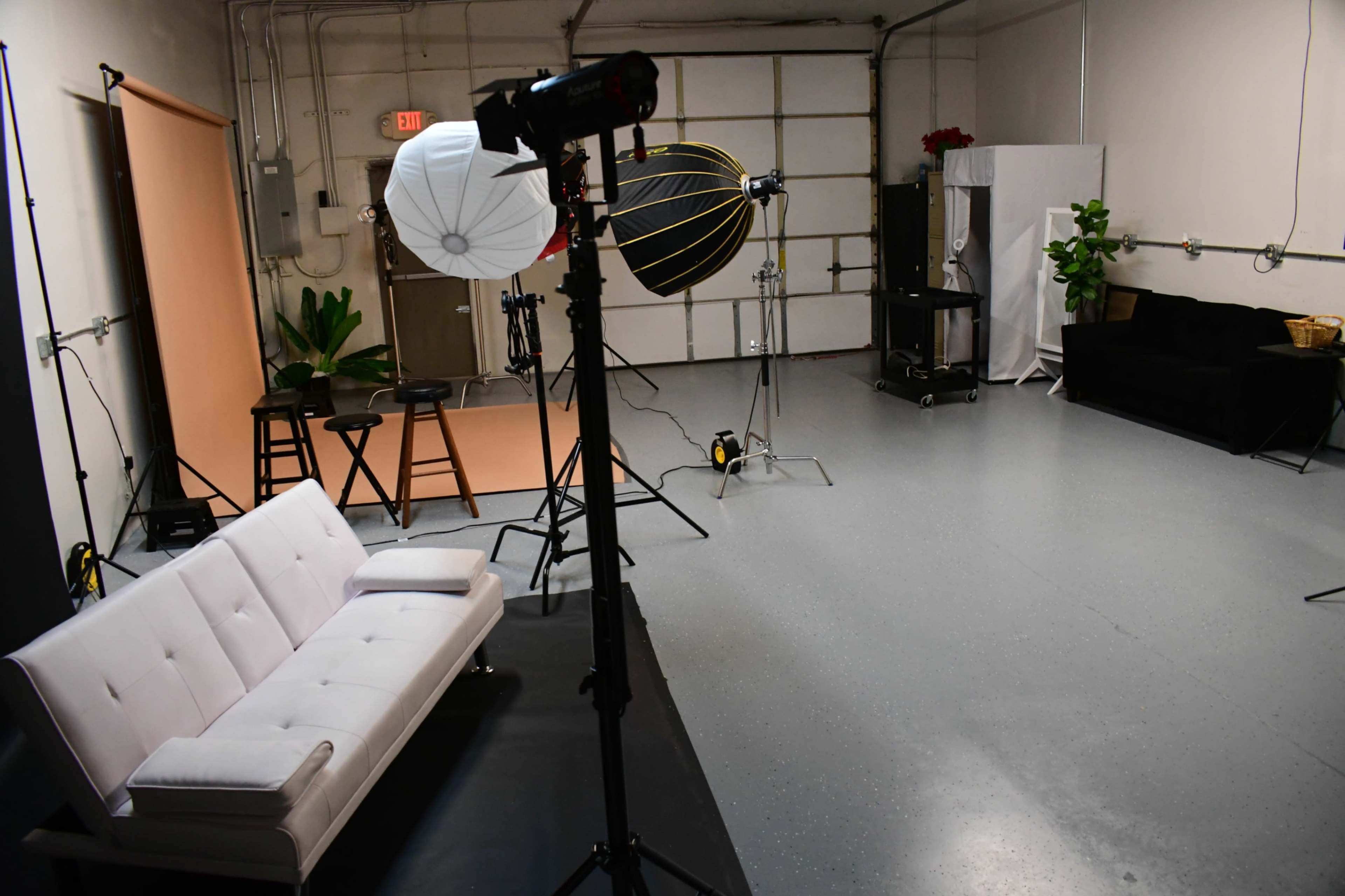 A photography studio equipped with lighting equipment, a white couch, and various props arranged on a gray floor.