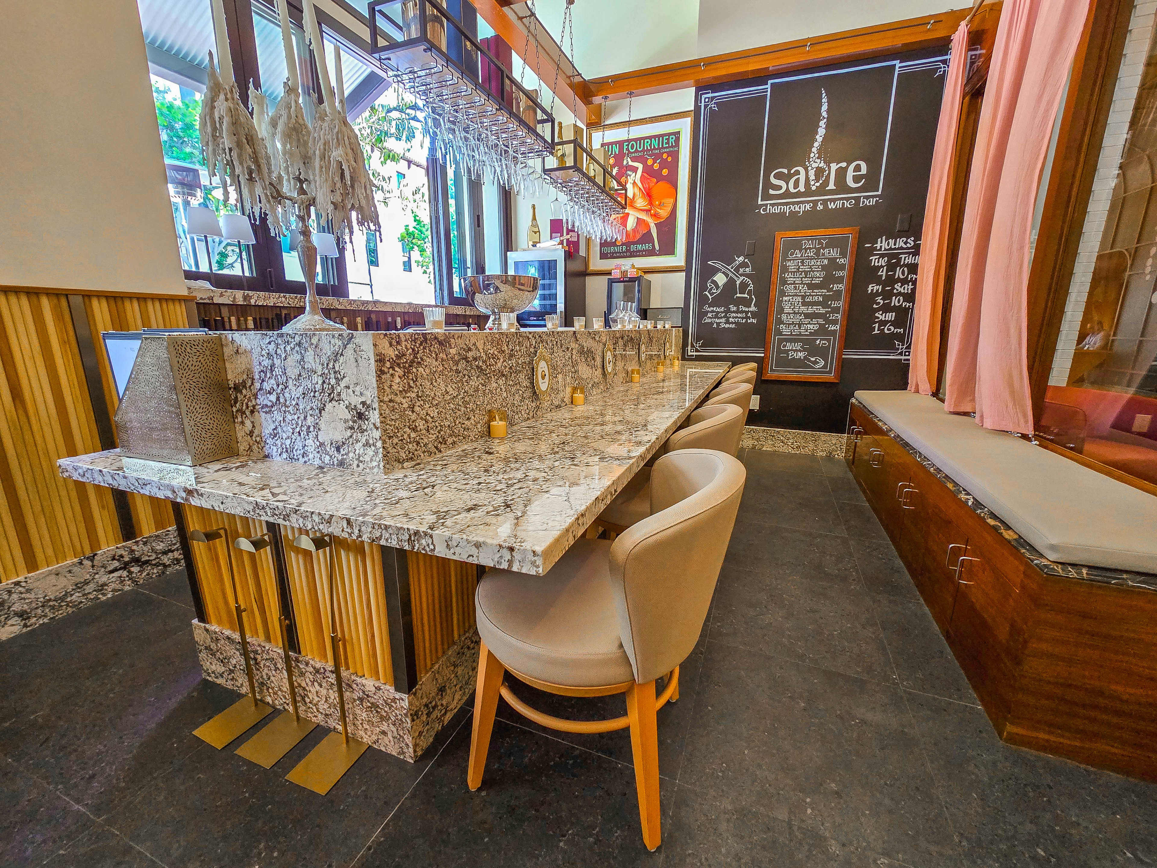 The image shows a modern restaurant interior with a granite bar, wooden accents, and a chalkboard menu displayed on the wall.