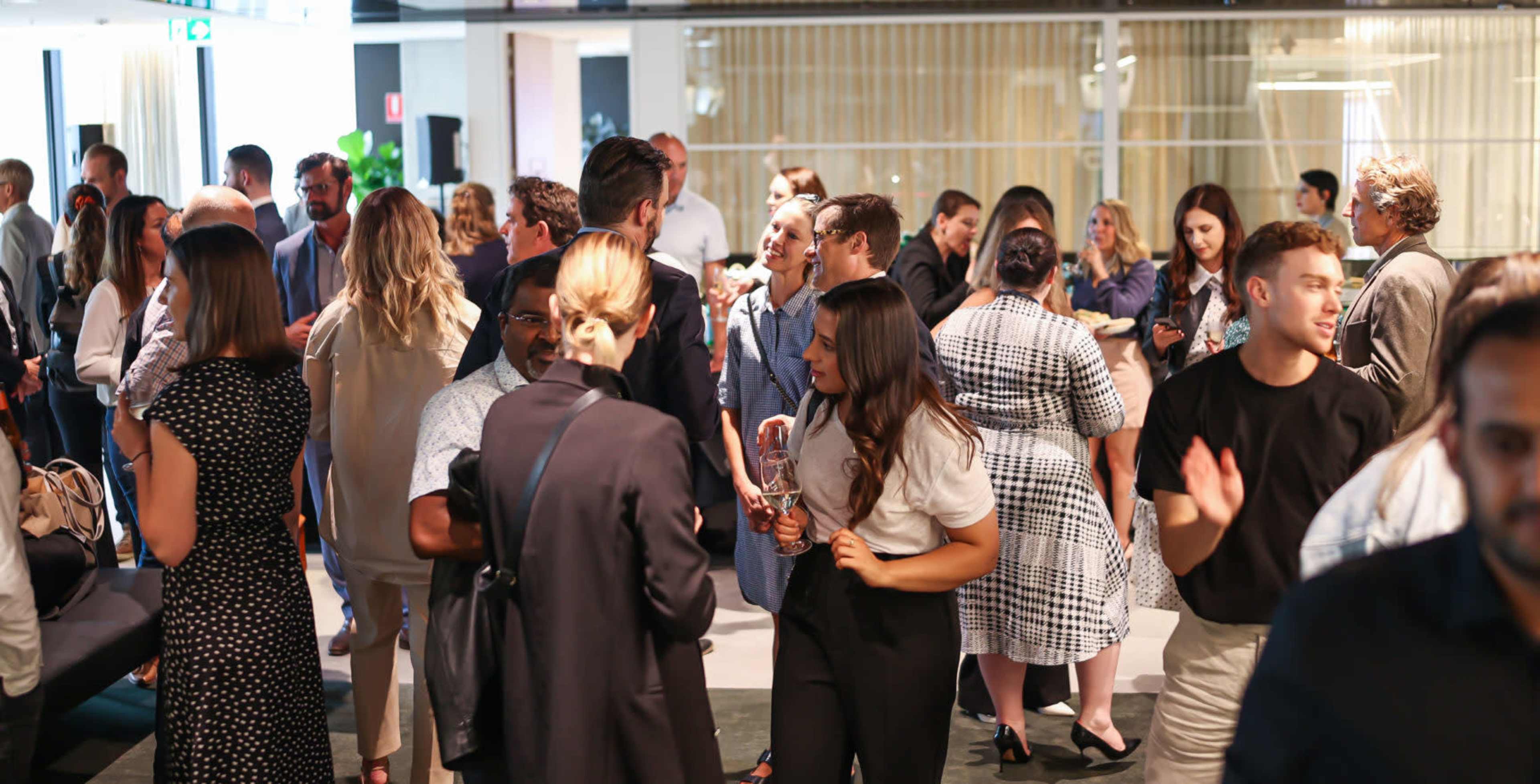 A large group of people socialize at a networking event in a modern indoor space.