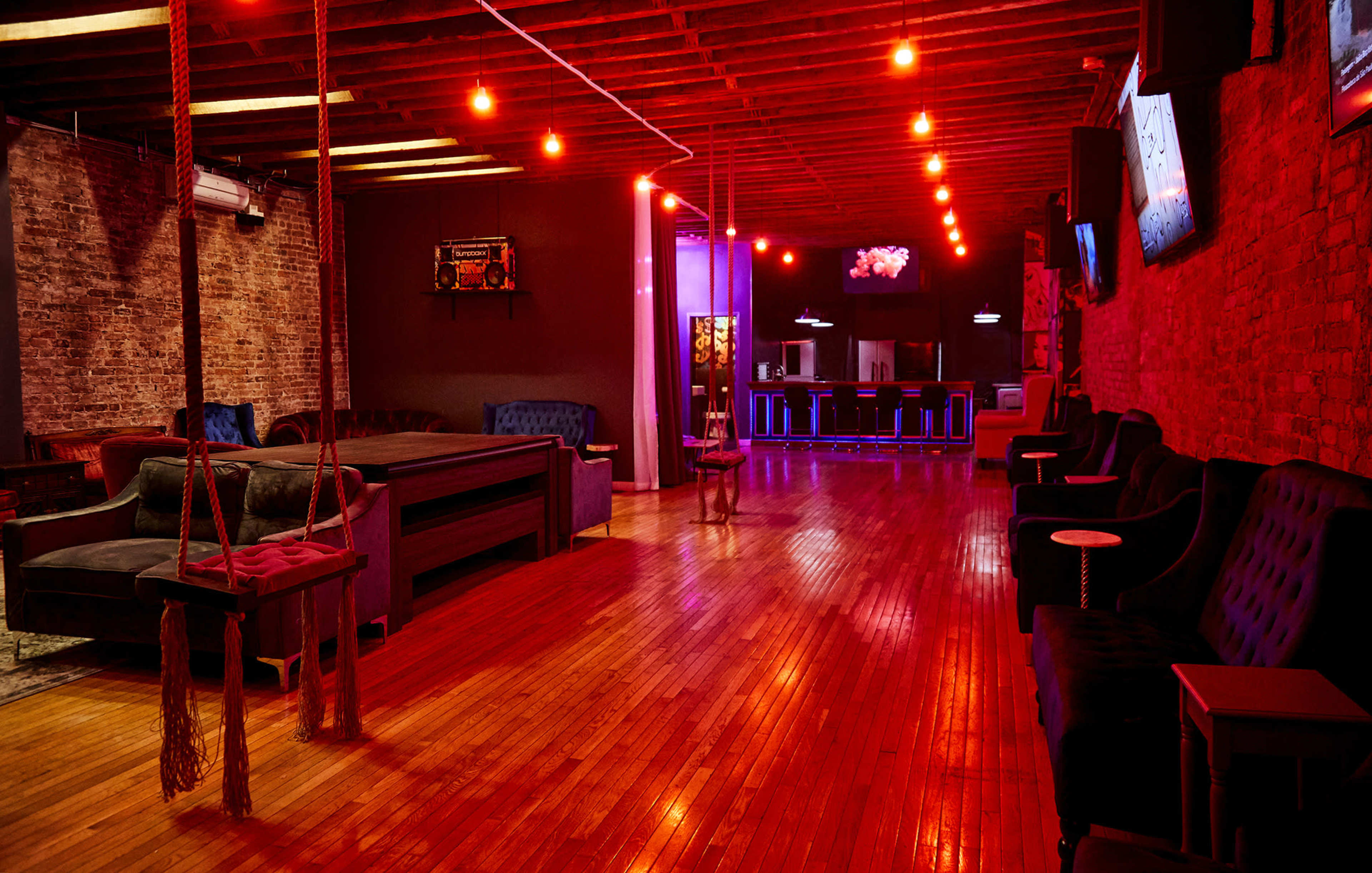 A spacious lounge area with hardwood floors, ambient red lighting, and a seating arrangement featuring couches and side tables.