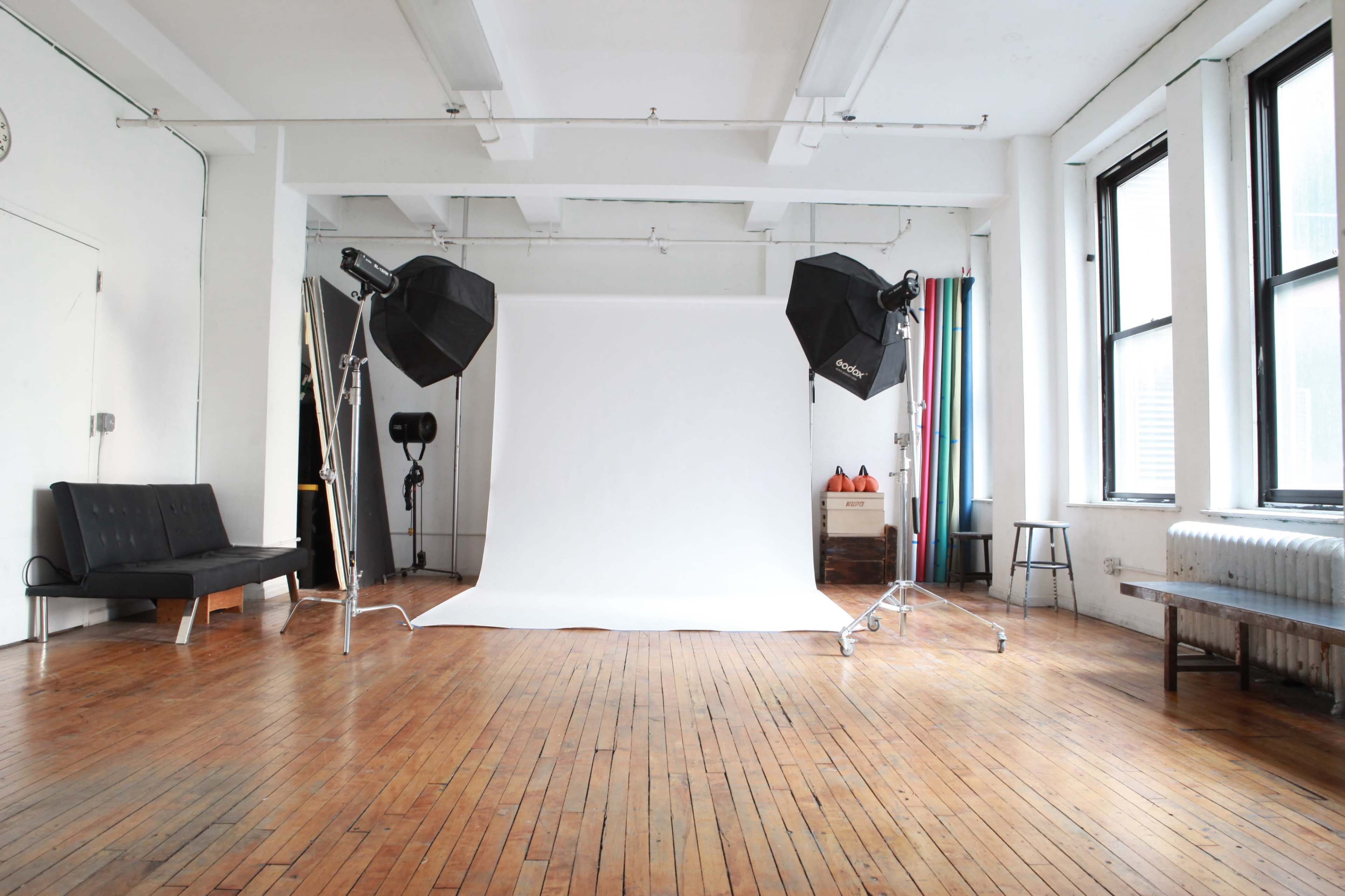 A photography studio with a white backdrop, studio lights, and wooden flooring.