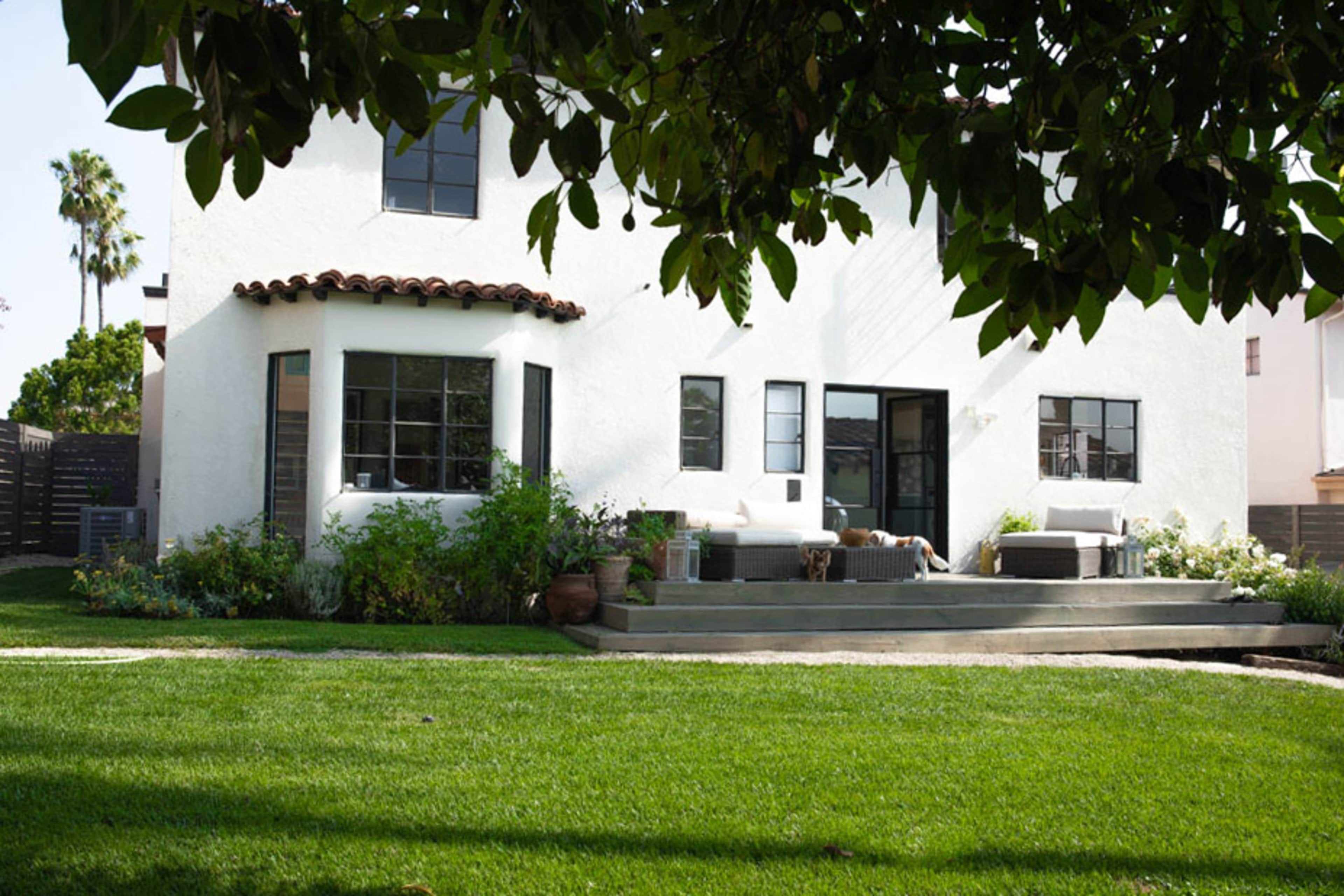 A two-story white house with a tiled roof, surrounded by a green lawn and patio seating.
