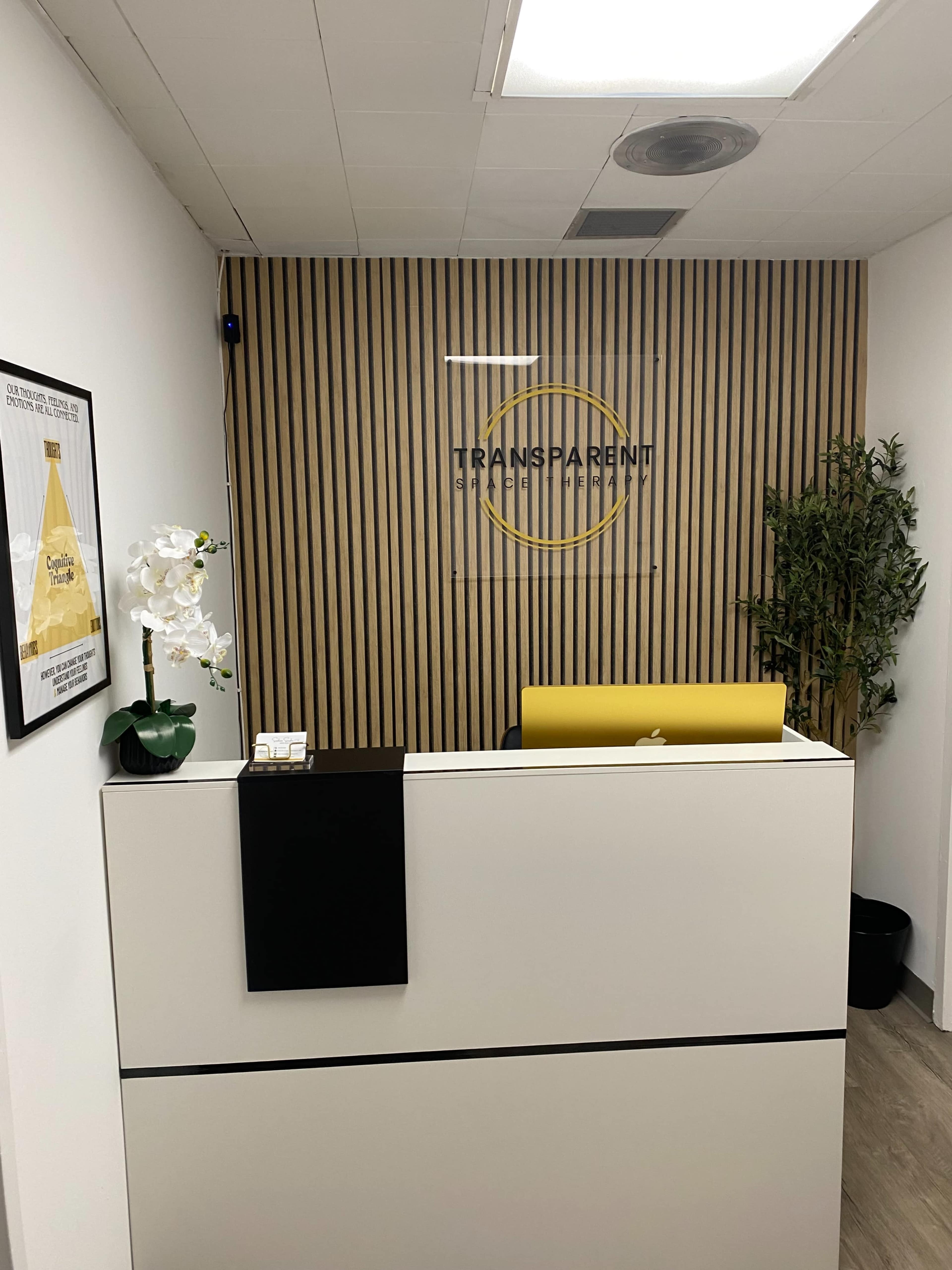 The image shows a modern reception area with a wooden slat feature wall, a white reception desk, and a yellow accent chair.