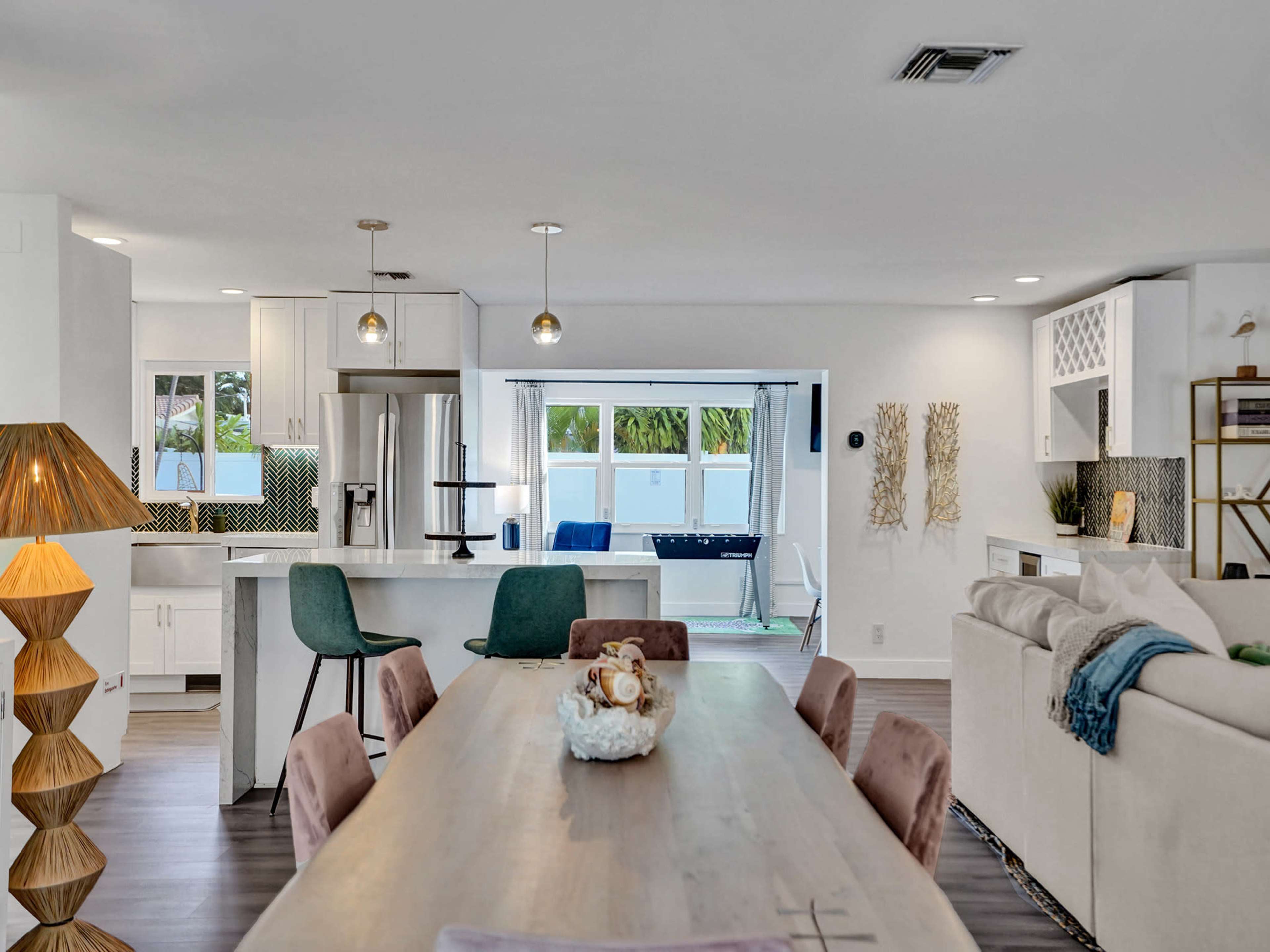 A modern open-concept living space featuring a dining table, kitchen with bar stools, and a living area with large windows.