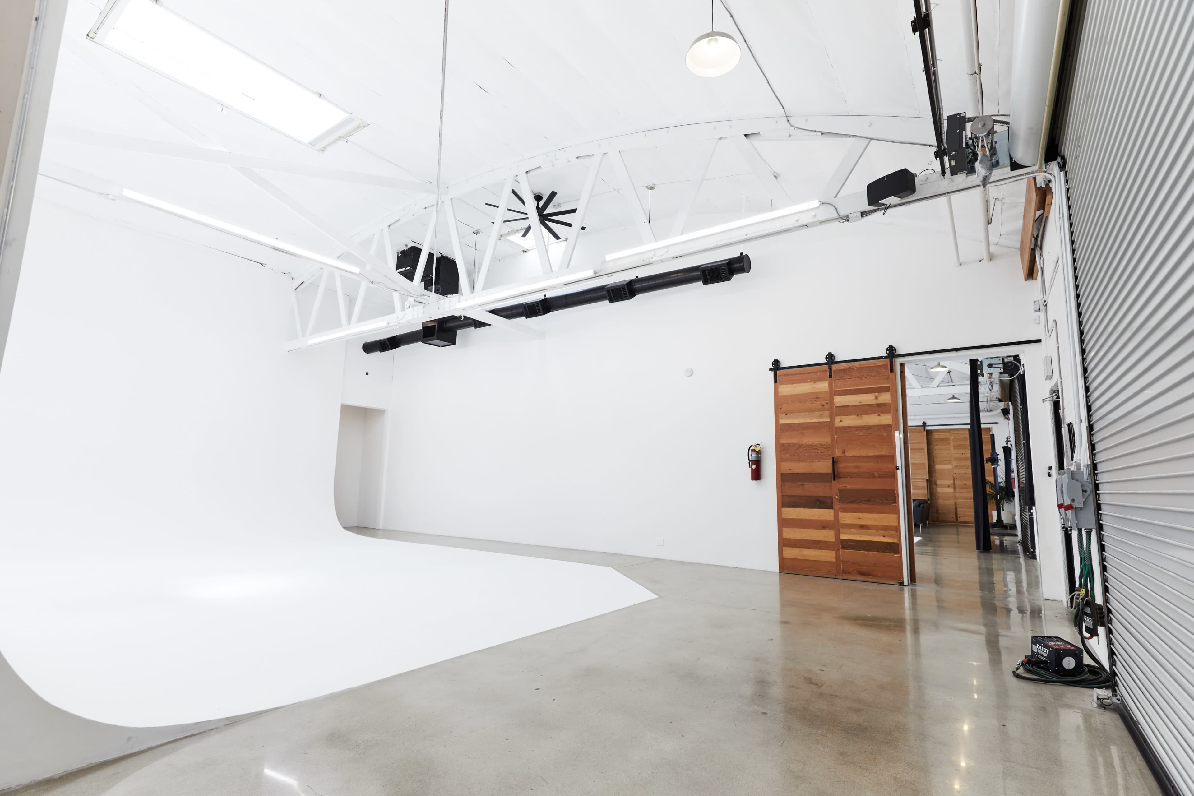 The image shows a spacious white studio with a seamless backdrop and large windows, featuring polished concrete floors and wooden sliding doors.