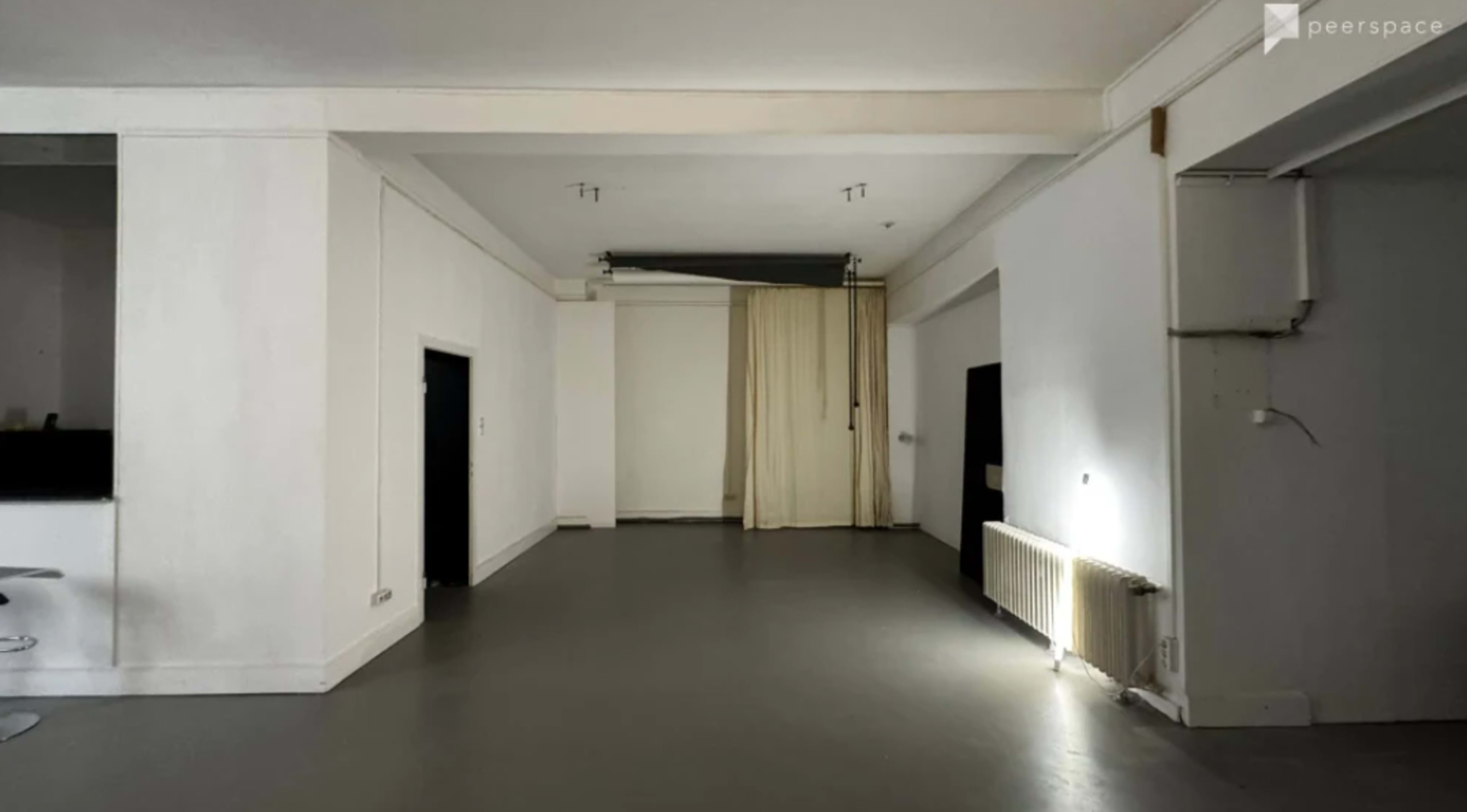 The image shows a spacious, empty room with white walls, a concrete floor, and curtains on one side.