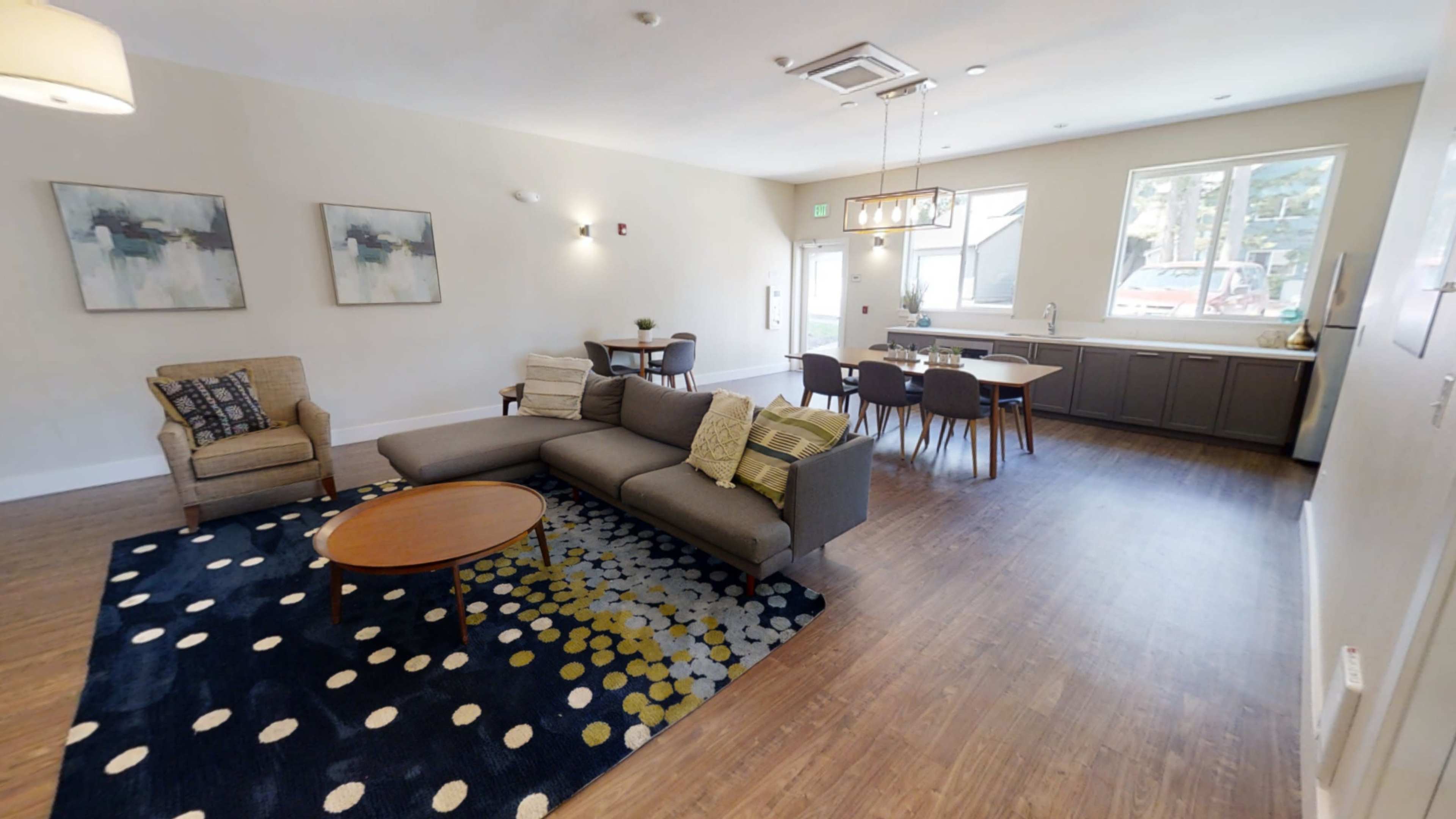 A modern living area with a seating arrangement, a dining table, and large windows providing natural light.