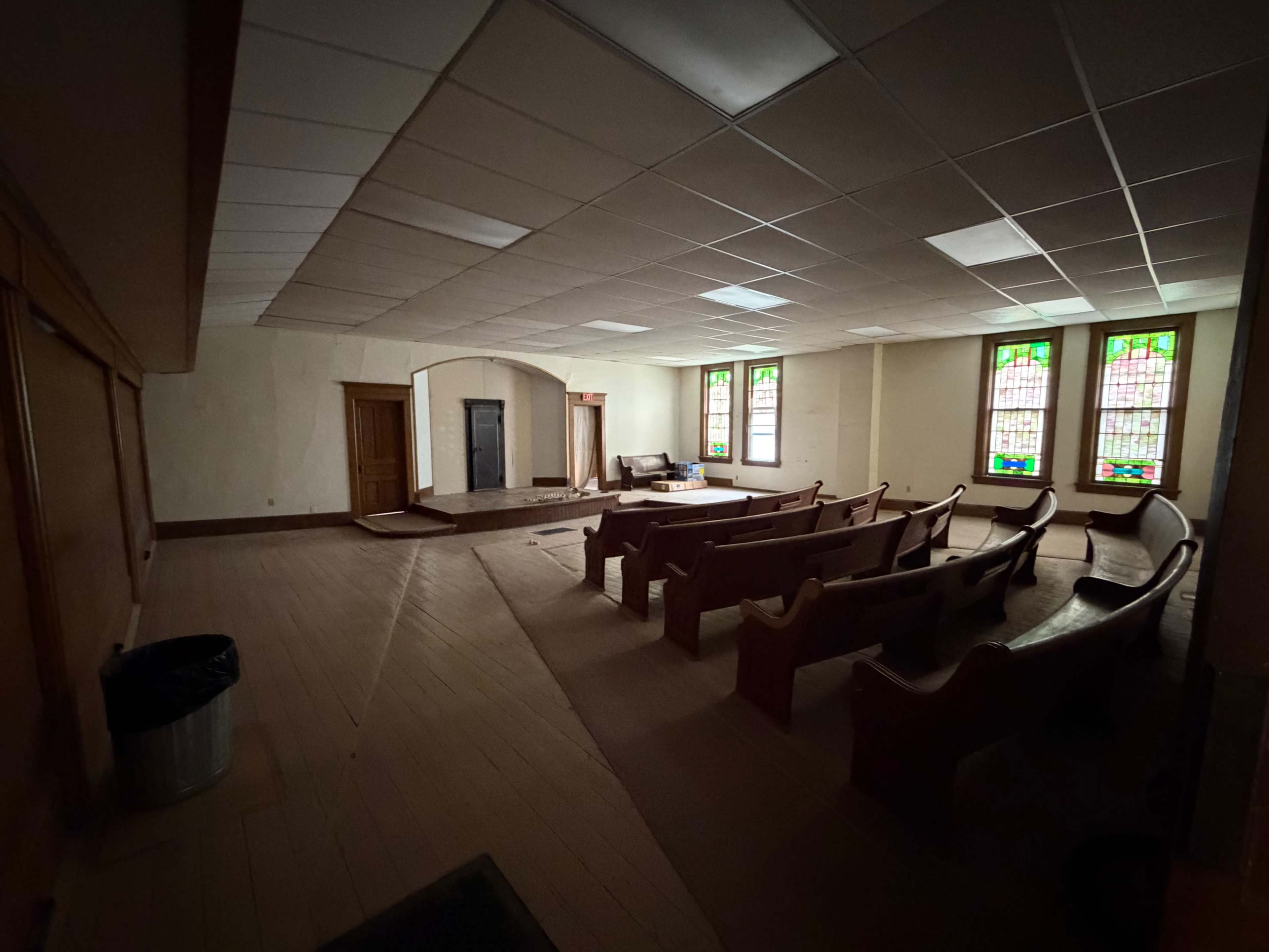 The image shows a vacant interior of a church, featuring wooden pews, stained glass windows, and an altar area.