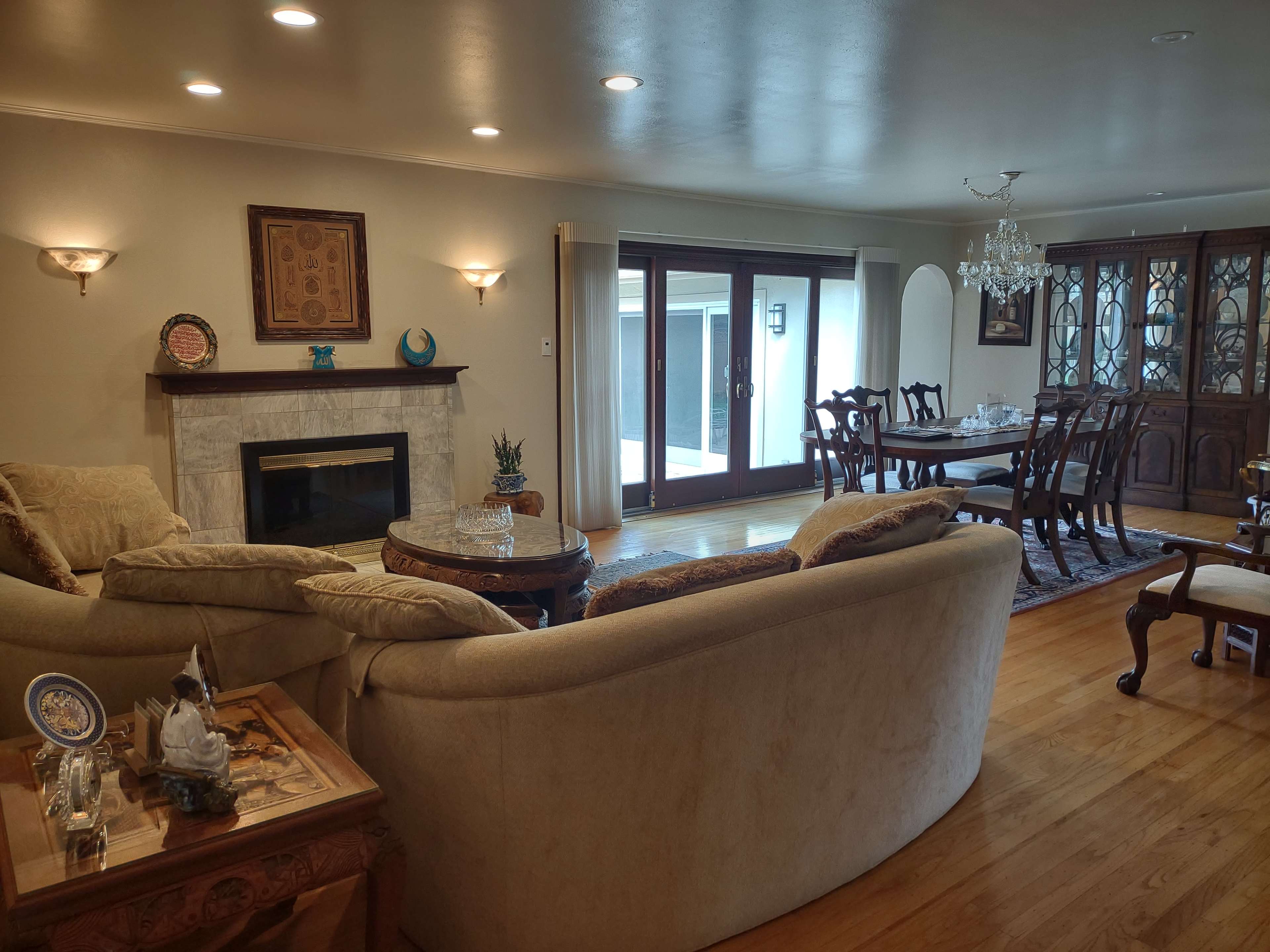A spacious living room with a beige sectional sofa, a fireplace, and a dining area featuring a wooden table and a glass-front cabinet.