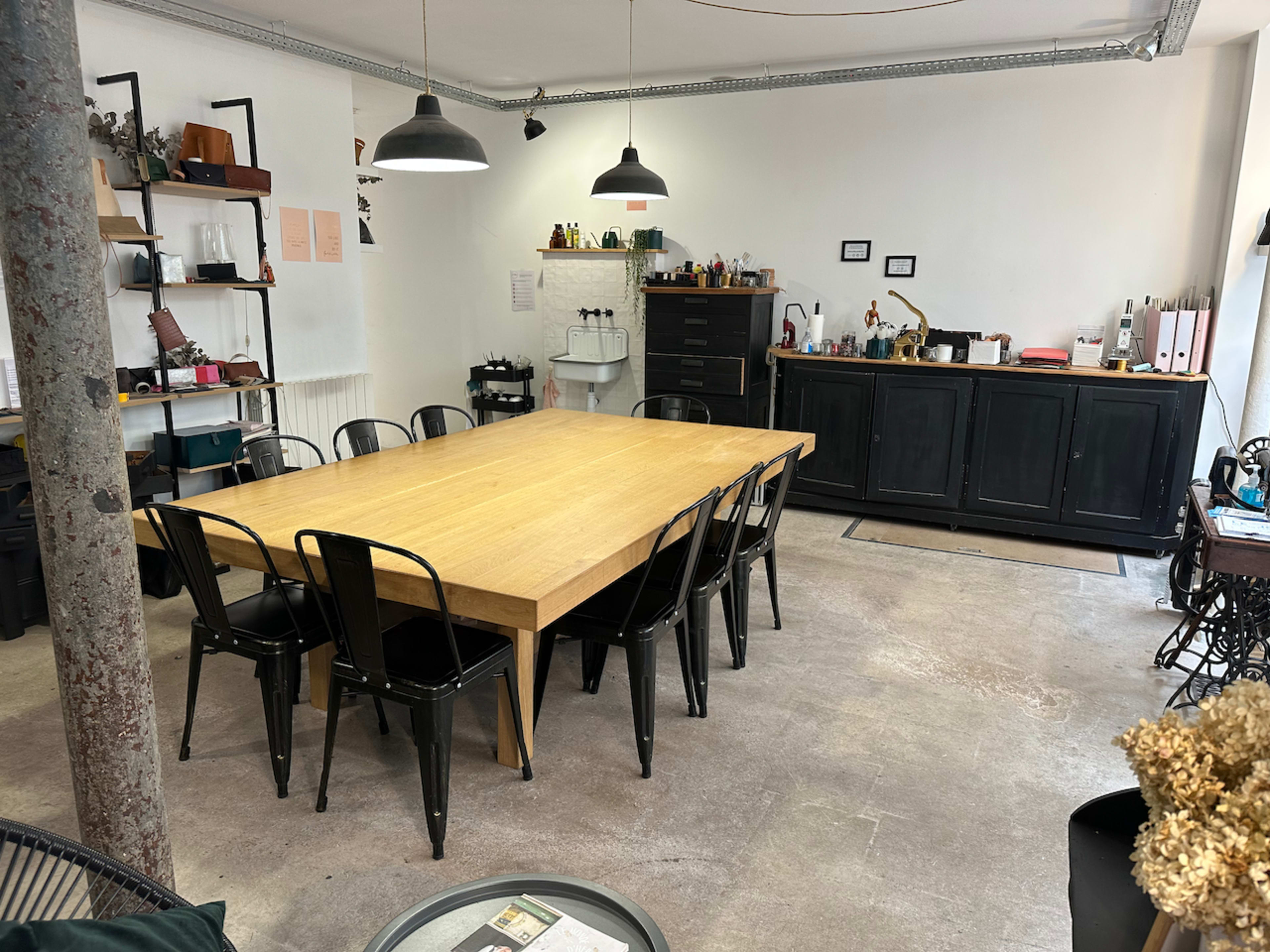 A spacious room features a large wooden table surrounded by black metal chairs, with shelves and cabinets against the walls.
