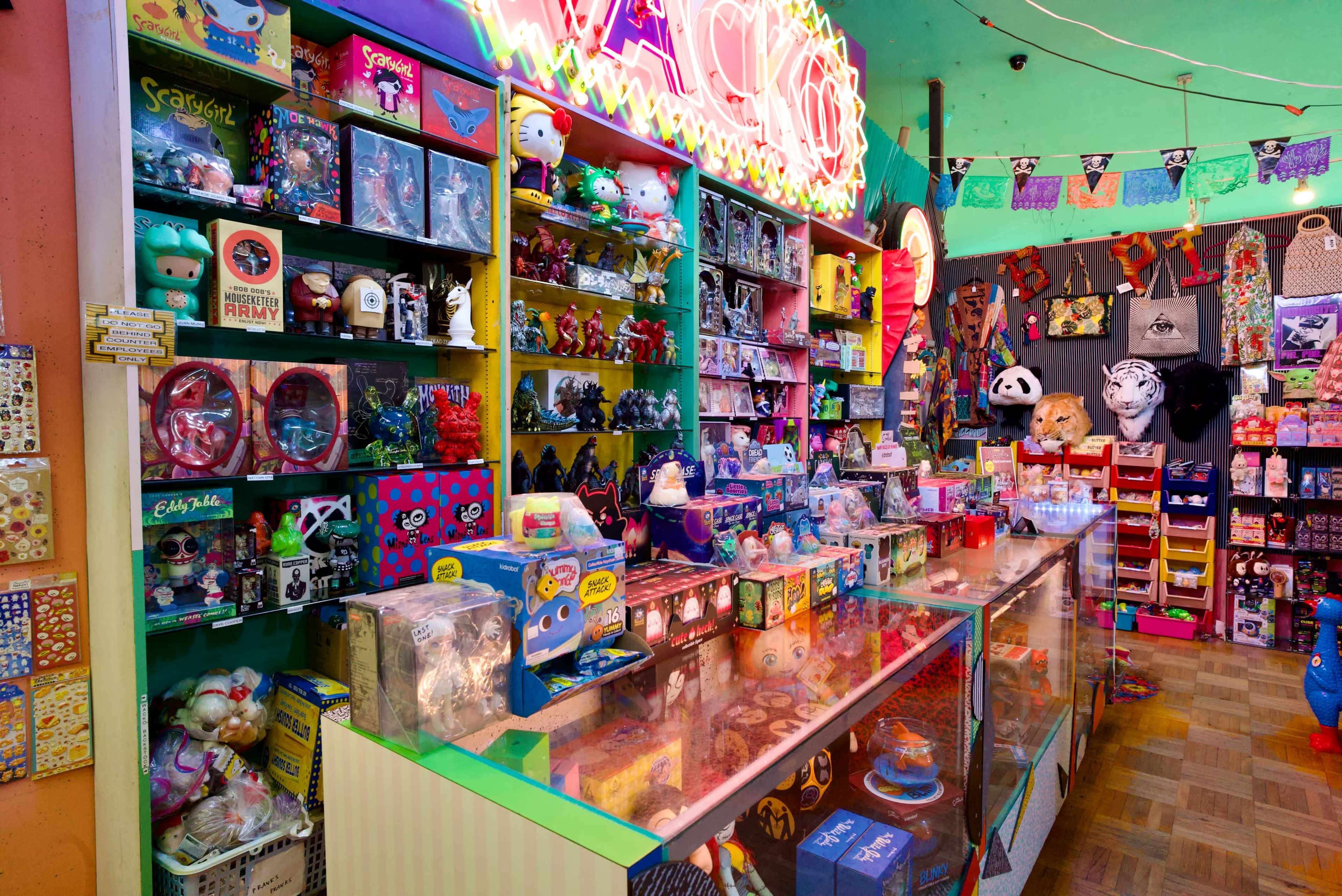 The image shows a vibrant toy store filled with colorful merchandise, including plush toys, figurines, and novelty items displayed on shelves and counters.