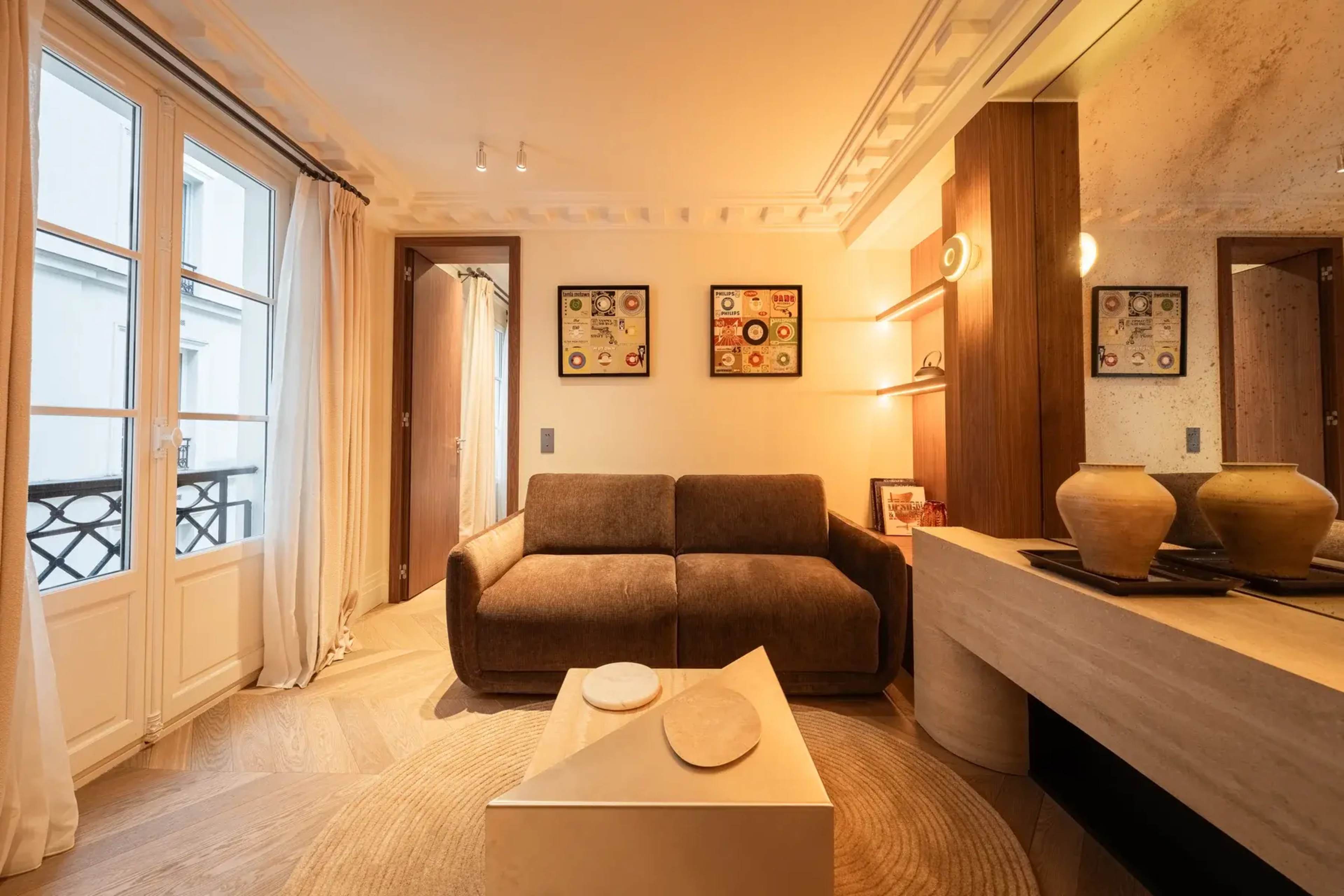 The image shows a modern living room with a brown sofa, a round area rug, a minimalist coffee table, and decorative elements on the walls.