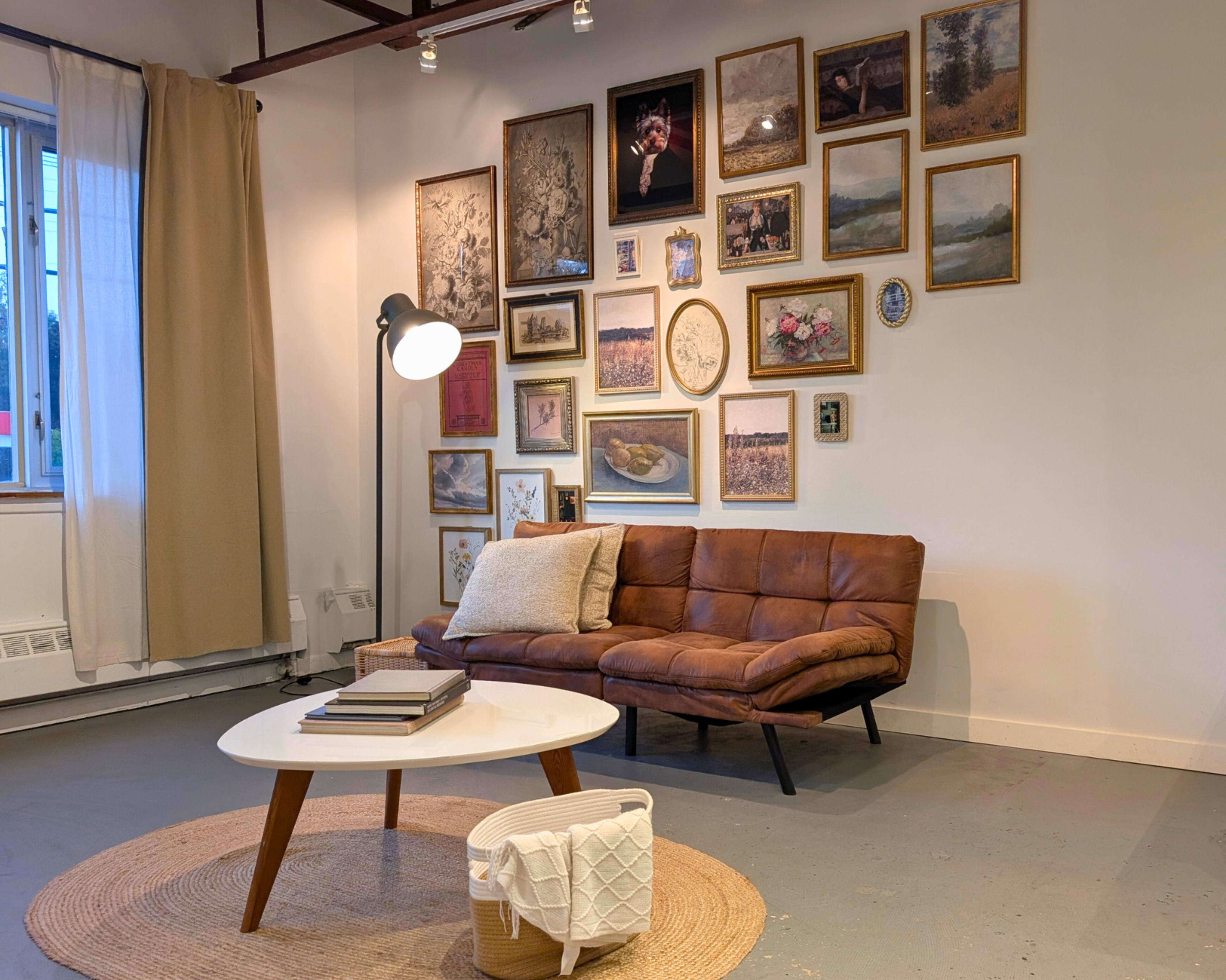 The image shows a cozy living area featuring a brown couch, a round coffee table, and a gallery wall with various framed artworks and photographs.