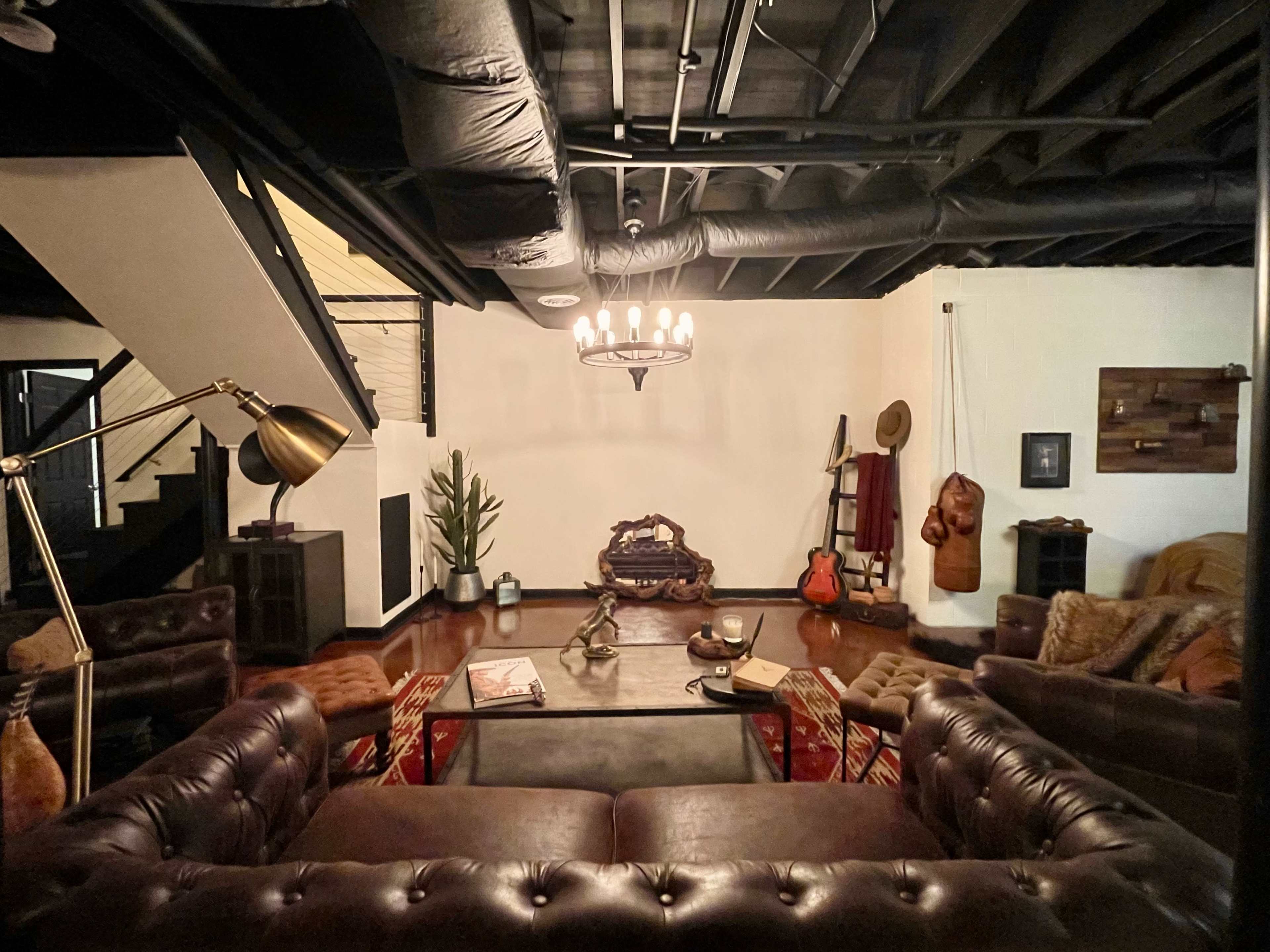 A stylish living room featuring a leather sofa set, a coffee table, a staircase, and various decorative elements including a guitar and a potted plant.