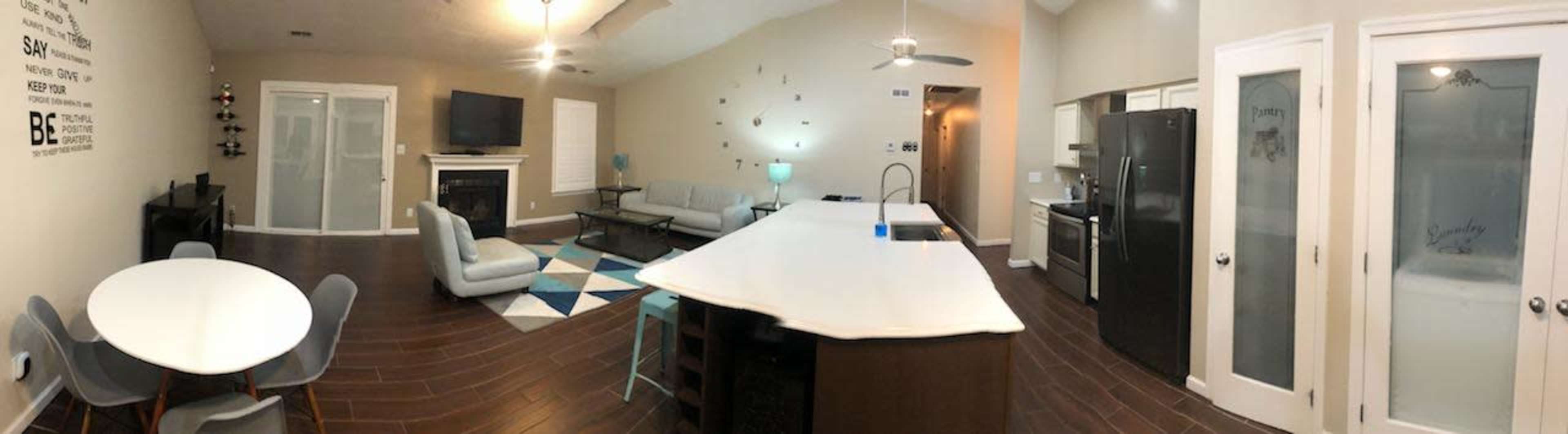 A panoramic view of a modern, open-concept living space featuring a kitchen island, dining table, and seating area with a television.