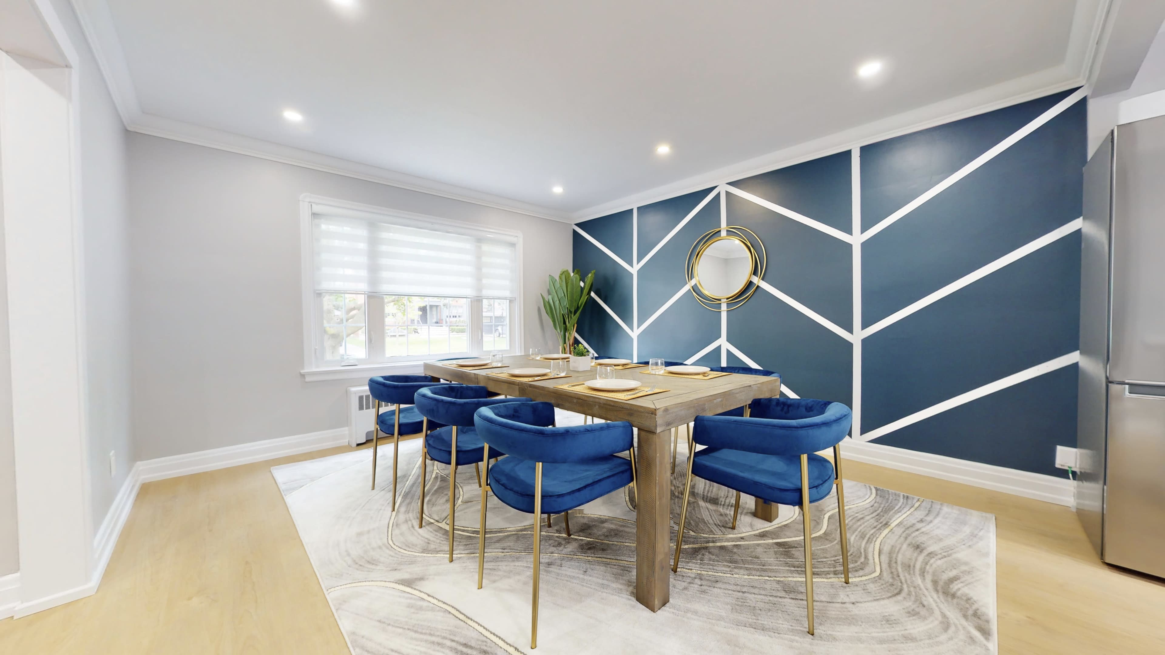 A dining room with a wooden table surrounded by blue chairs, set against a geometric blue and white wall design.