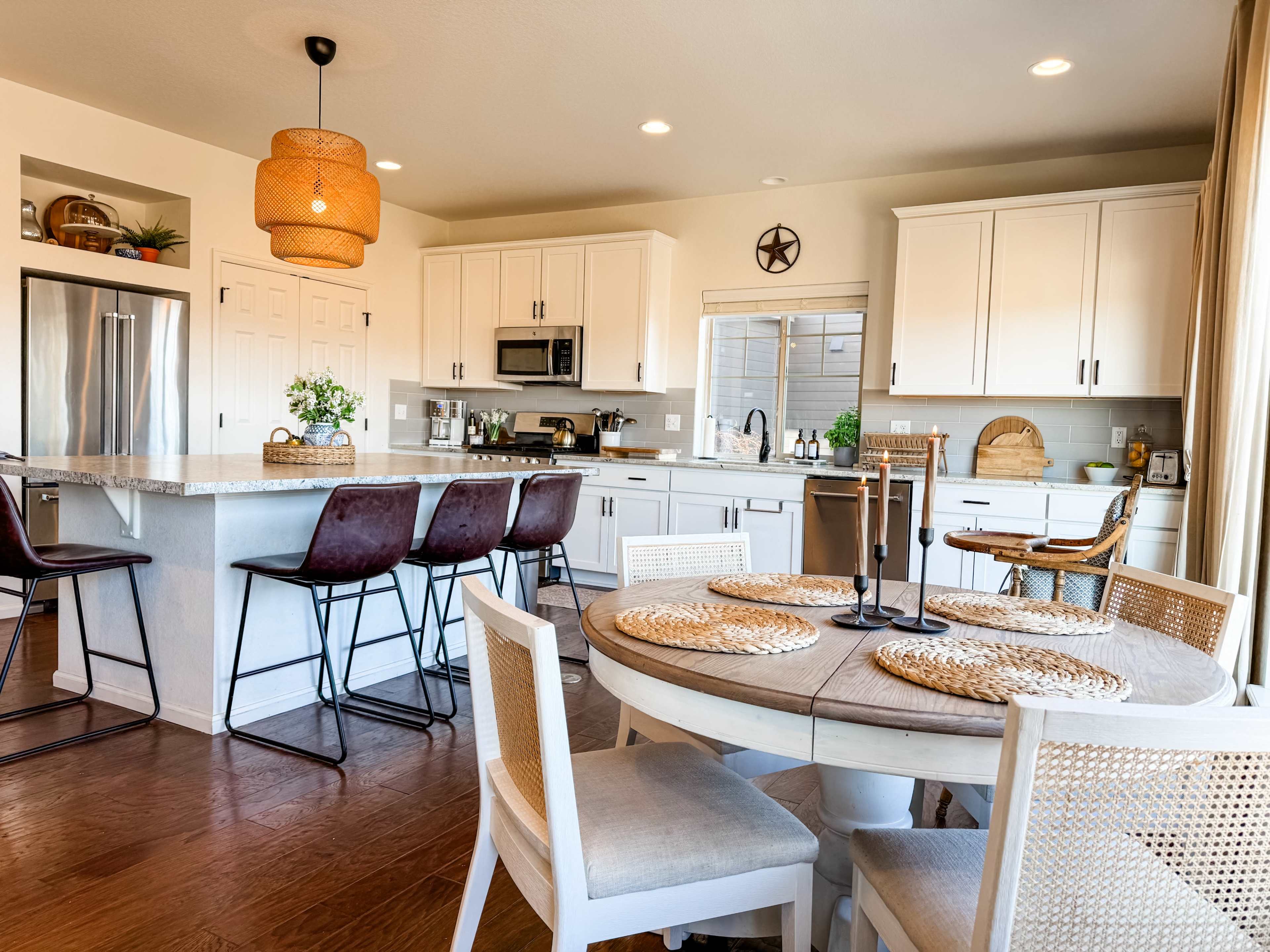 The image shows a modern kitchen with white cabinets, a central island with bar stools, and a dining table set with woven placemats.