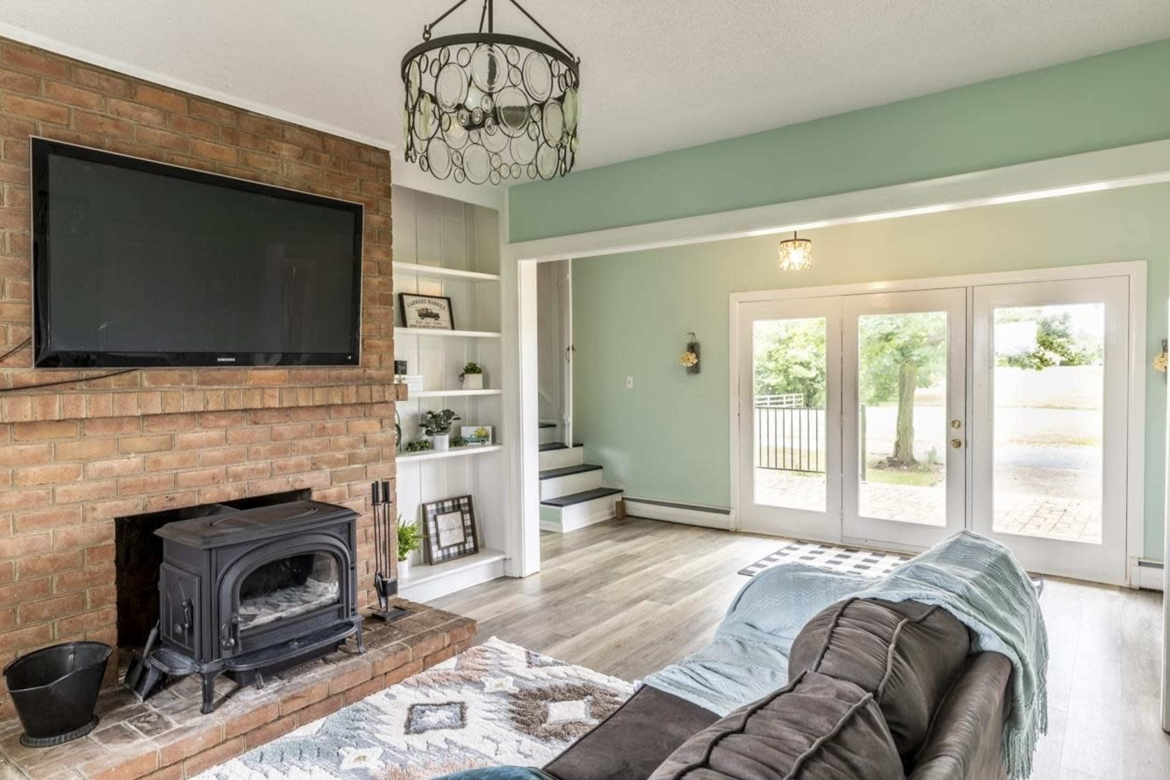 A living room with a brick fireplace, a mounted television, and a set of large glass doors leading to an outdoor area.