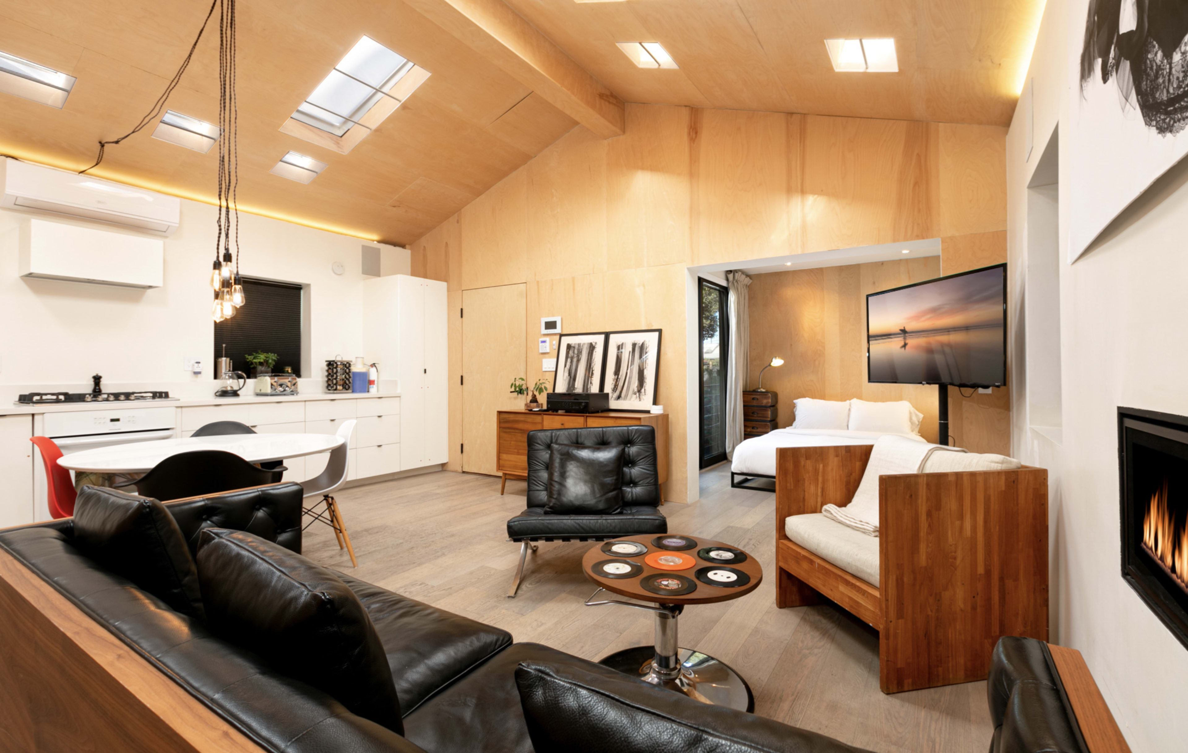 A modern, open-concept living space features a kitchen, seating area, and bedroom, with wooden accents and large windows.