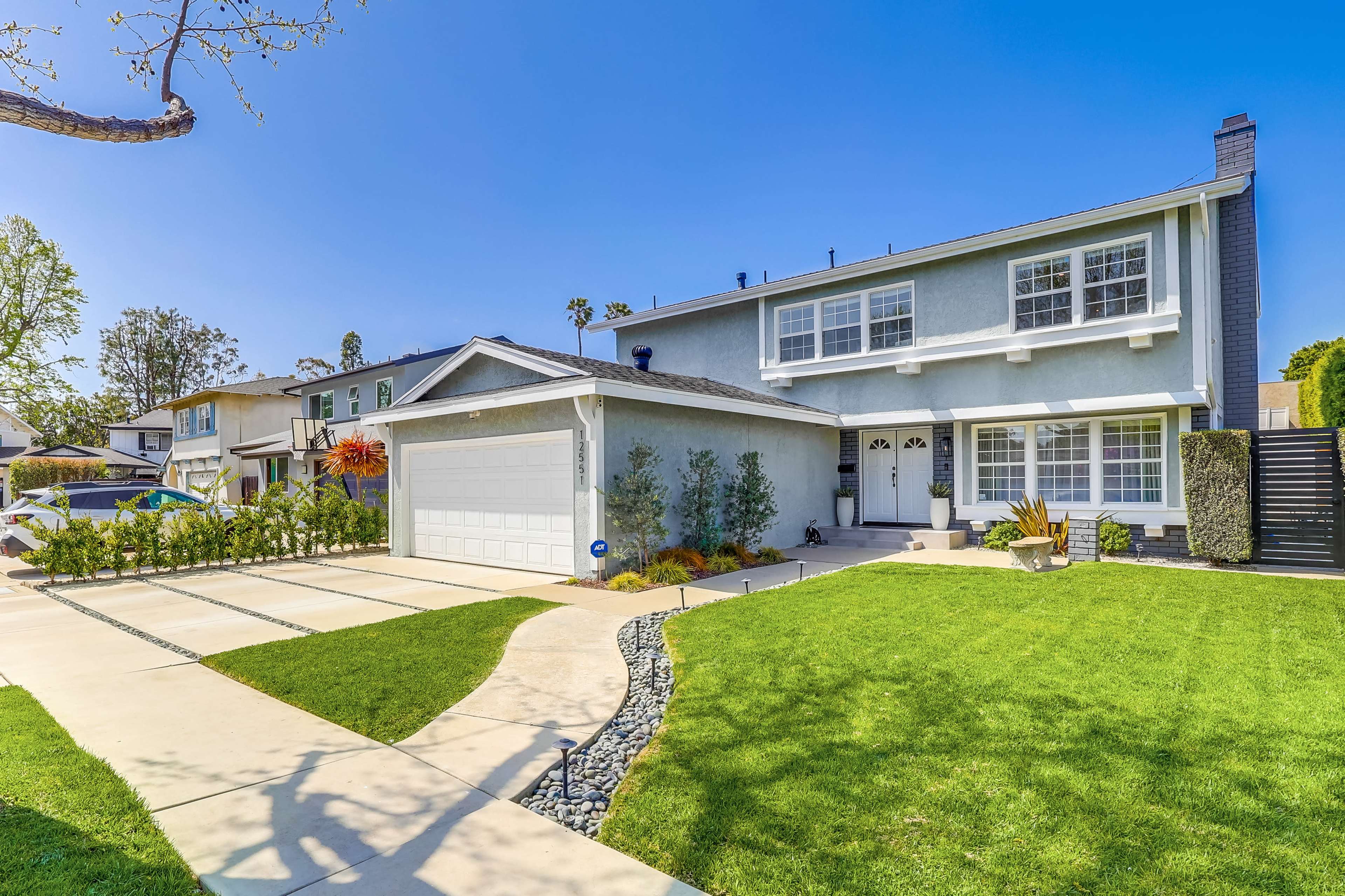 A two-story house with a green lawn and a concrete driveway is situated on a quiet suburban street.