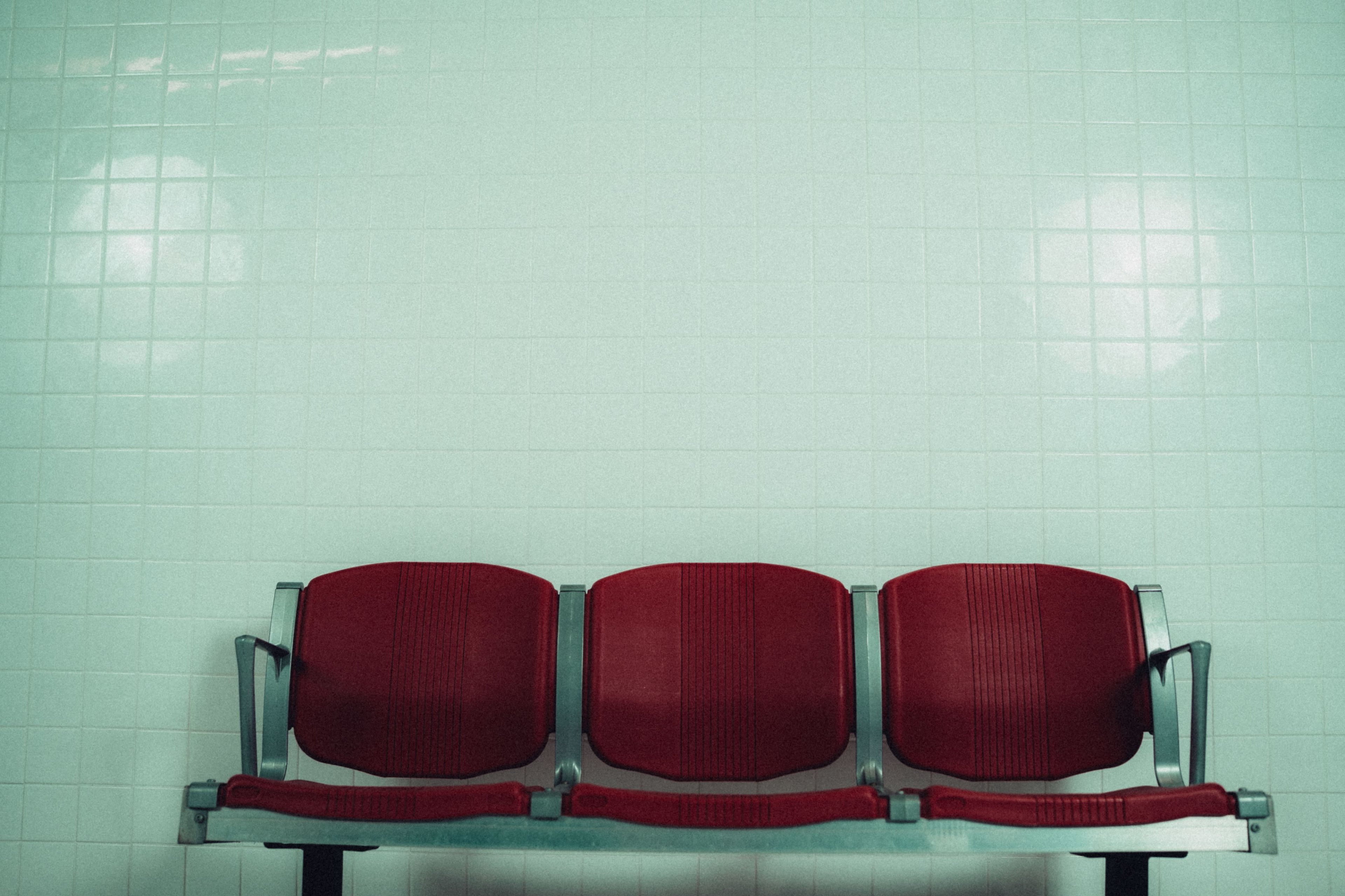 A row of three red seats is positioned against a pale green tiled wall.