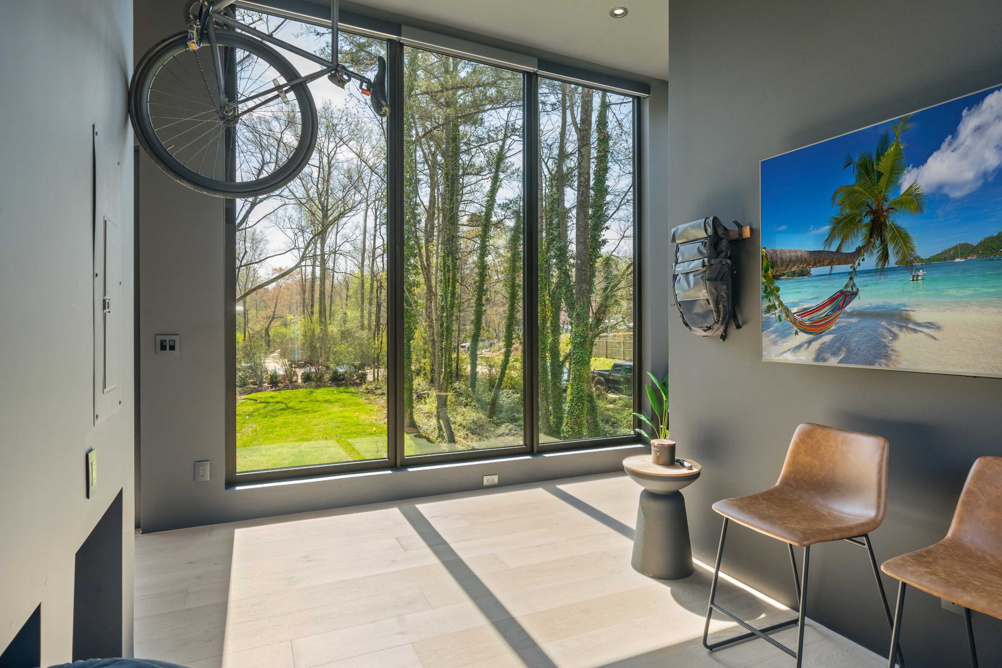 A modern room features large windows overlooking a green landscape, with a bicycle mounted on the wall and minimalist furniture.