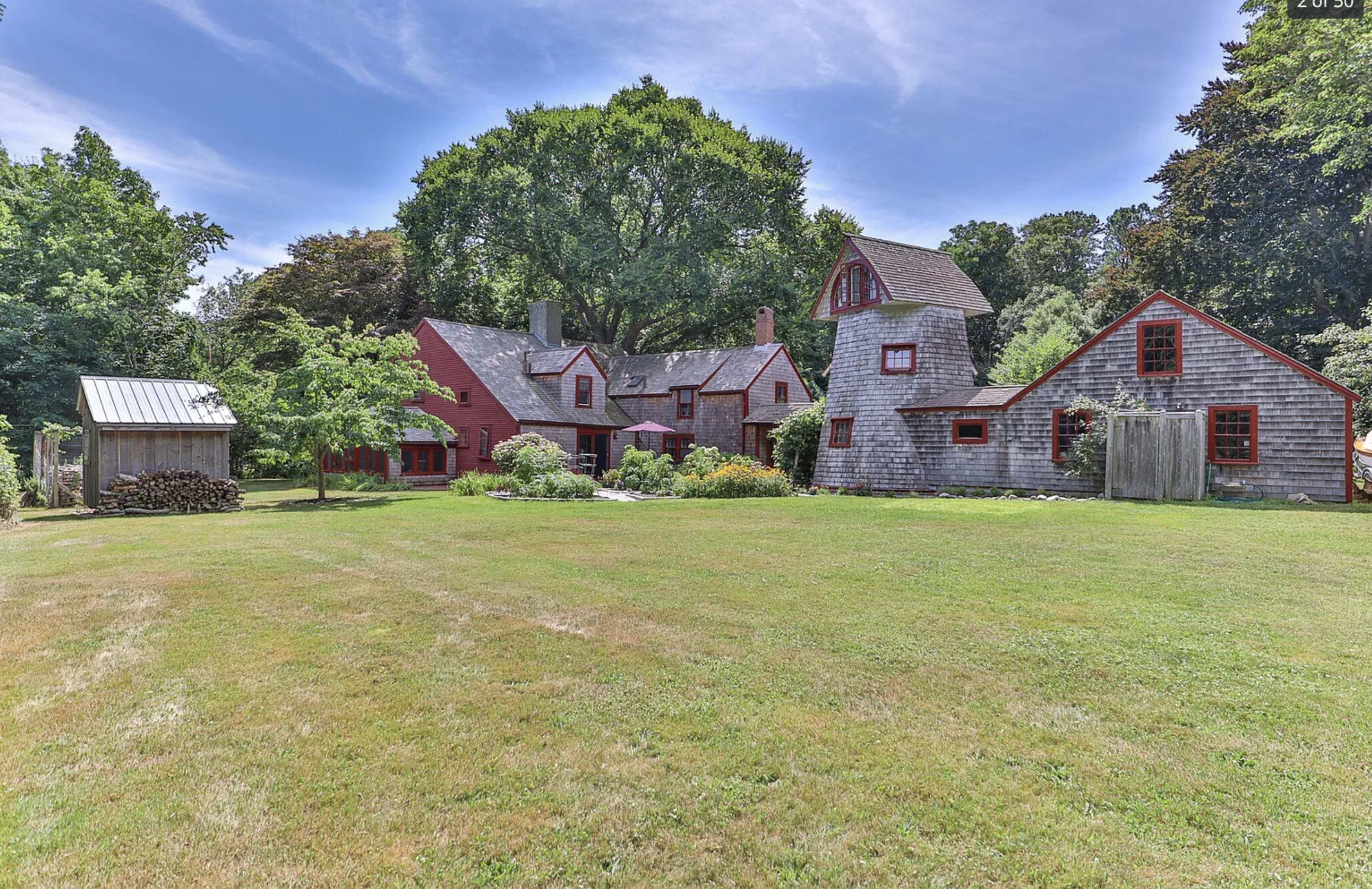 A large, multi-structure property featuring a red main house, a barn-like building, and a well-maintained yard with green grass and trees.