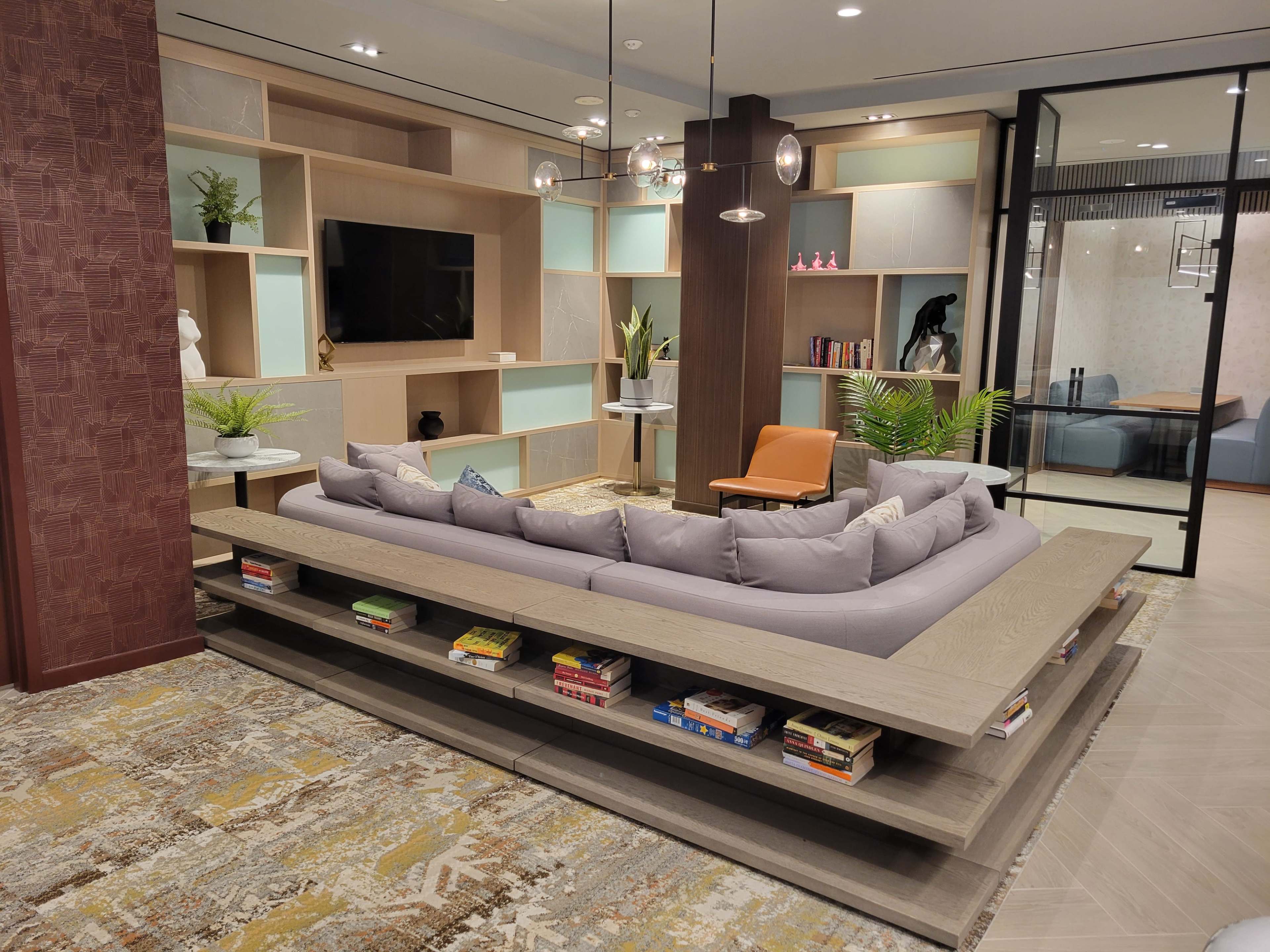 A modern living area with a large, low wooden seating structure surrounded by bookshelves, a television, and contemporary decor elements.
