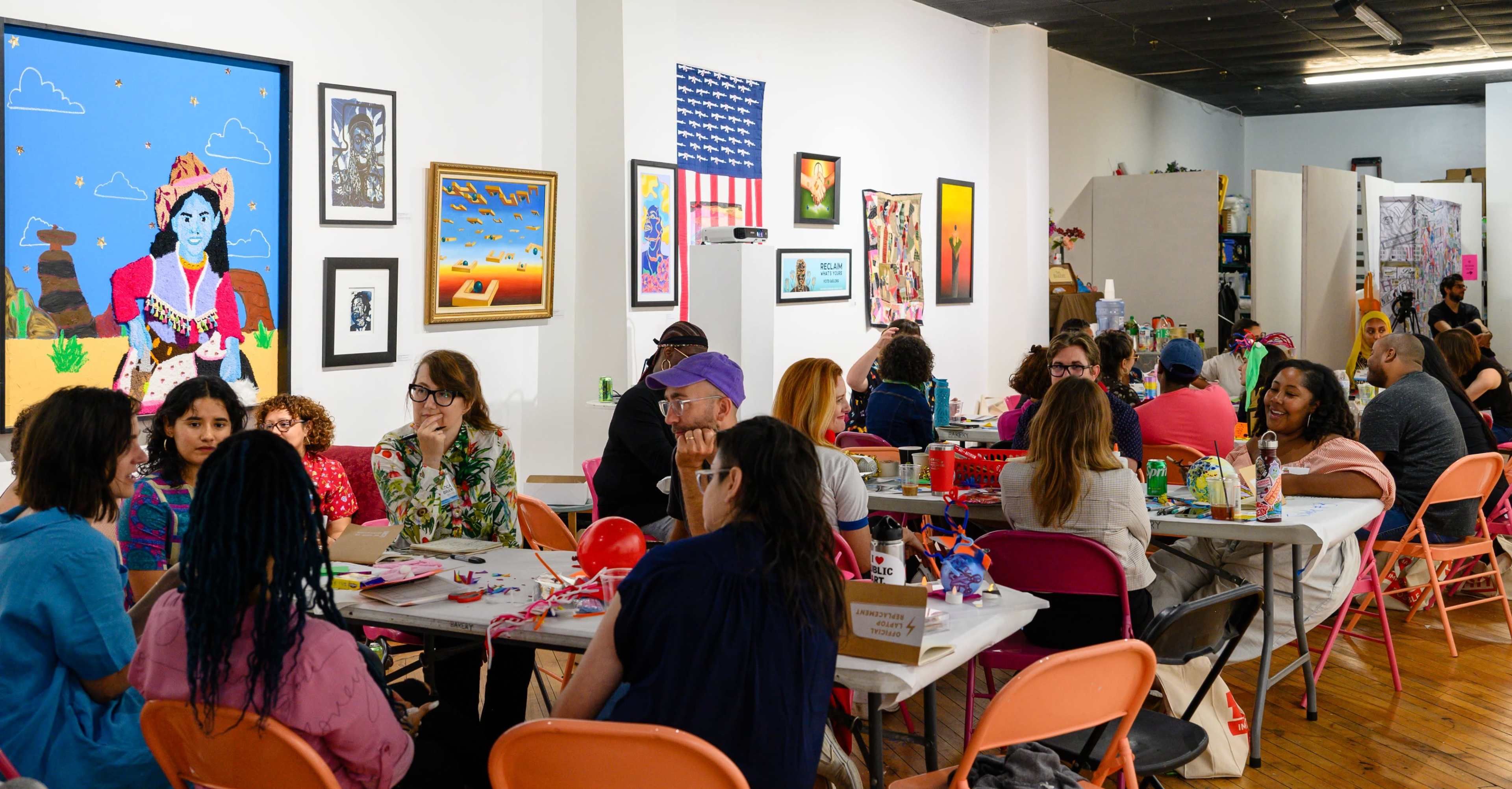 A lively art studio filled with people engaged in creative activities at tables, surrounded by colorful artwork on the walls.