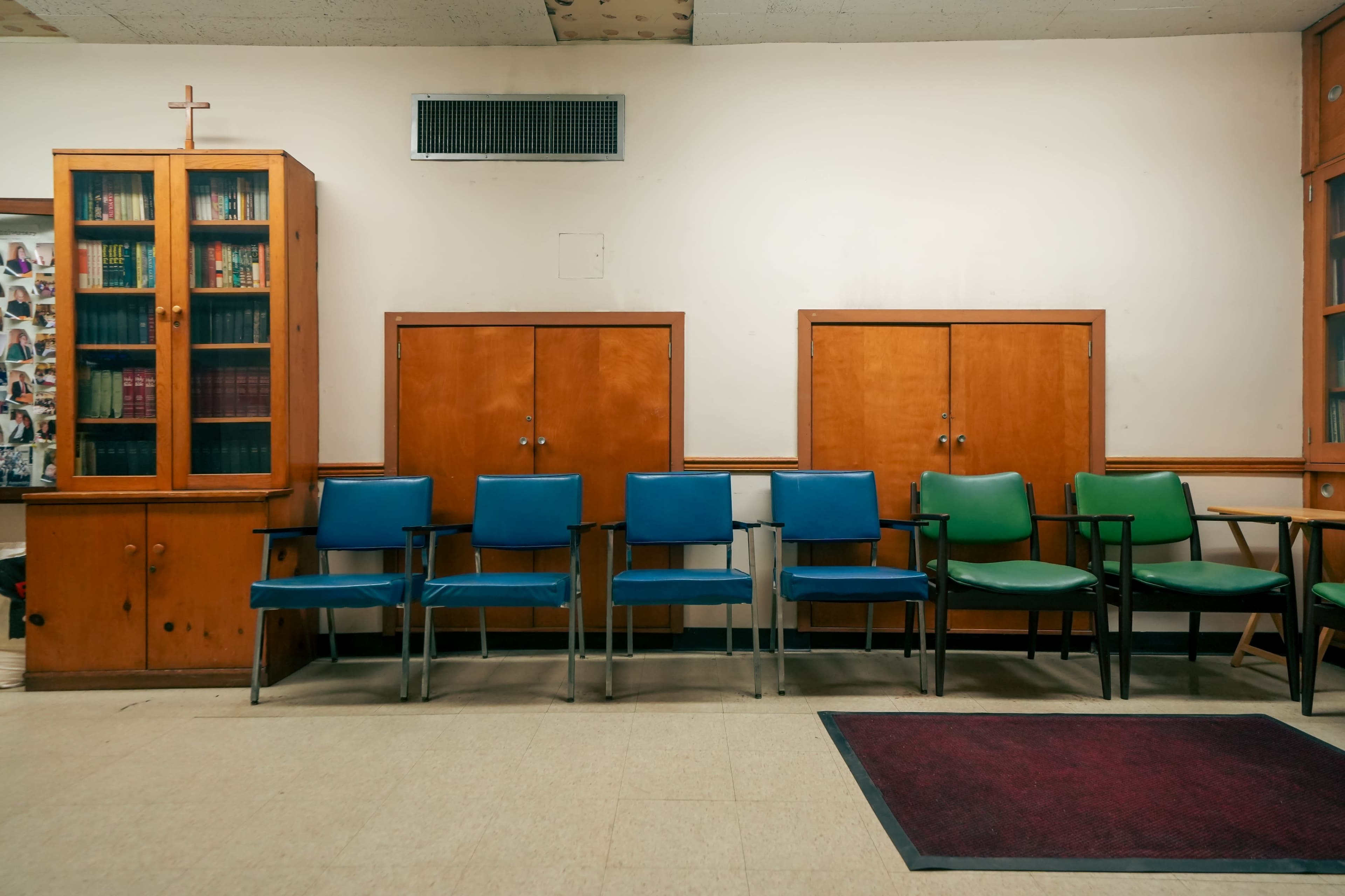 The image shows a waiting area with a row of chairs in various colors and a wooden bookshelf against the wall.