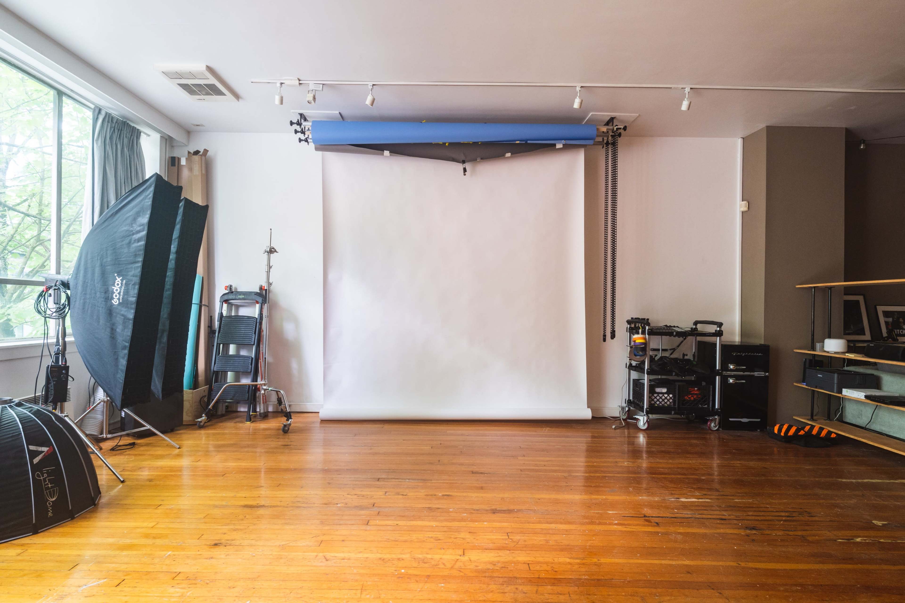 A spacious studio with hardwood floors features a white backdrop setup and various photography equipment along the walls.