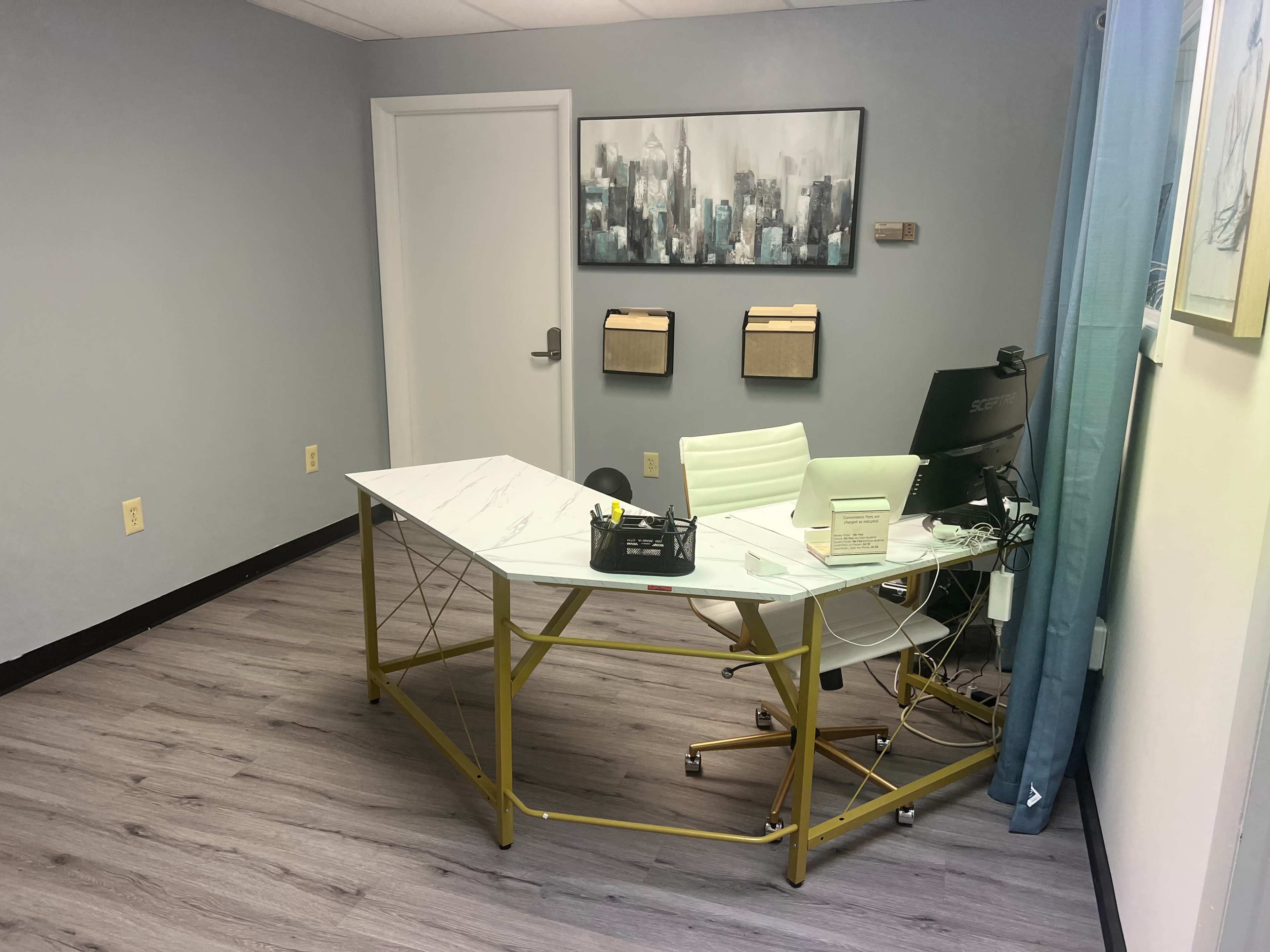 A modern office space featuring a marble-top desk, a white chair, and a computer setup against a blue wall with abstract artwork.