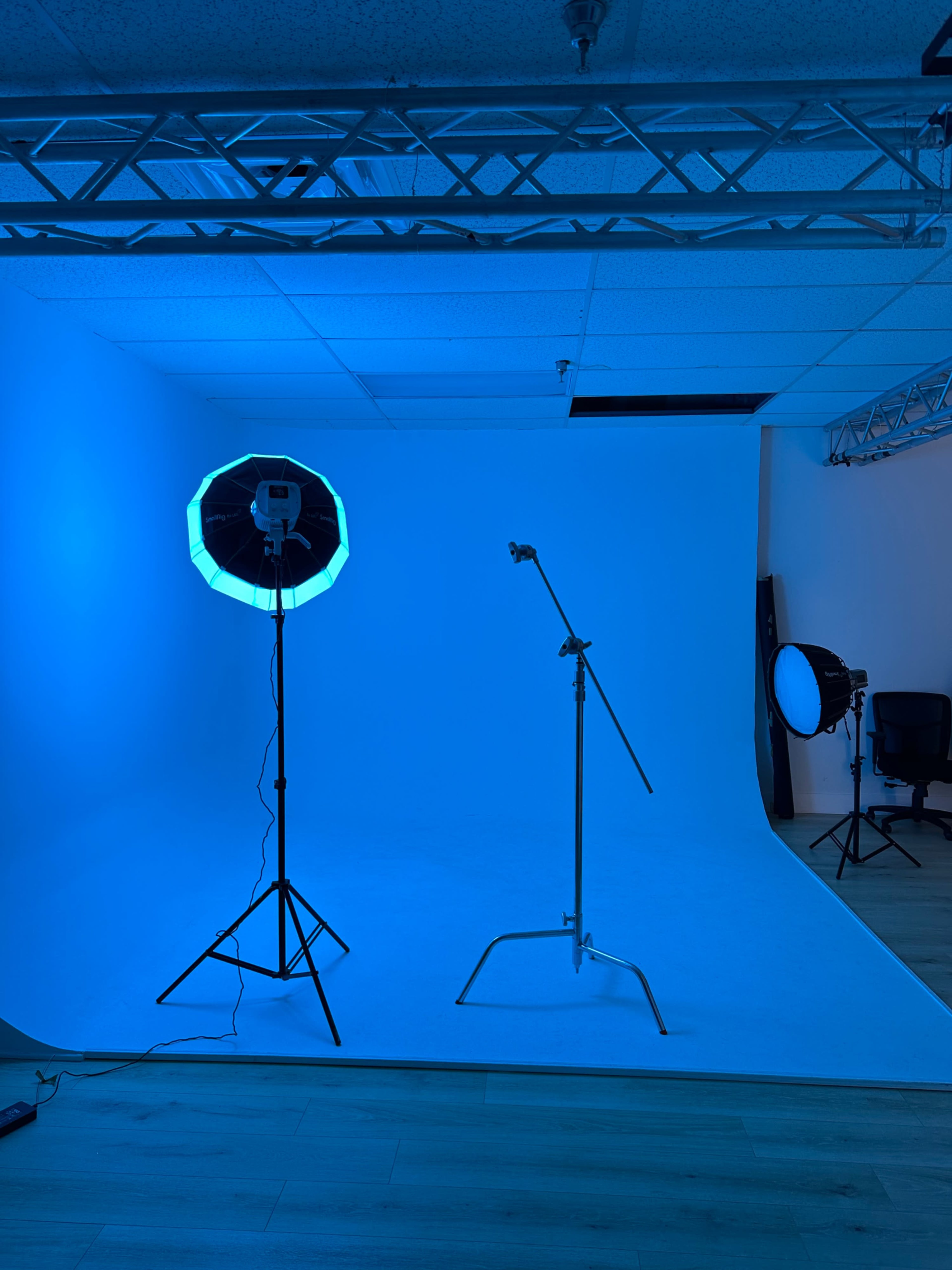A photography studio features a blue backdrop, softbox light, and a light stand on a wooden floor.