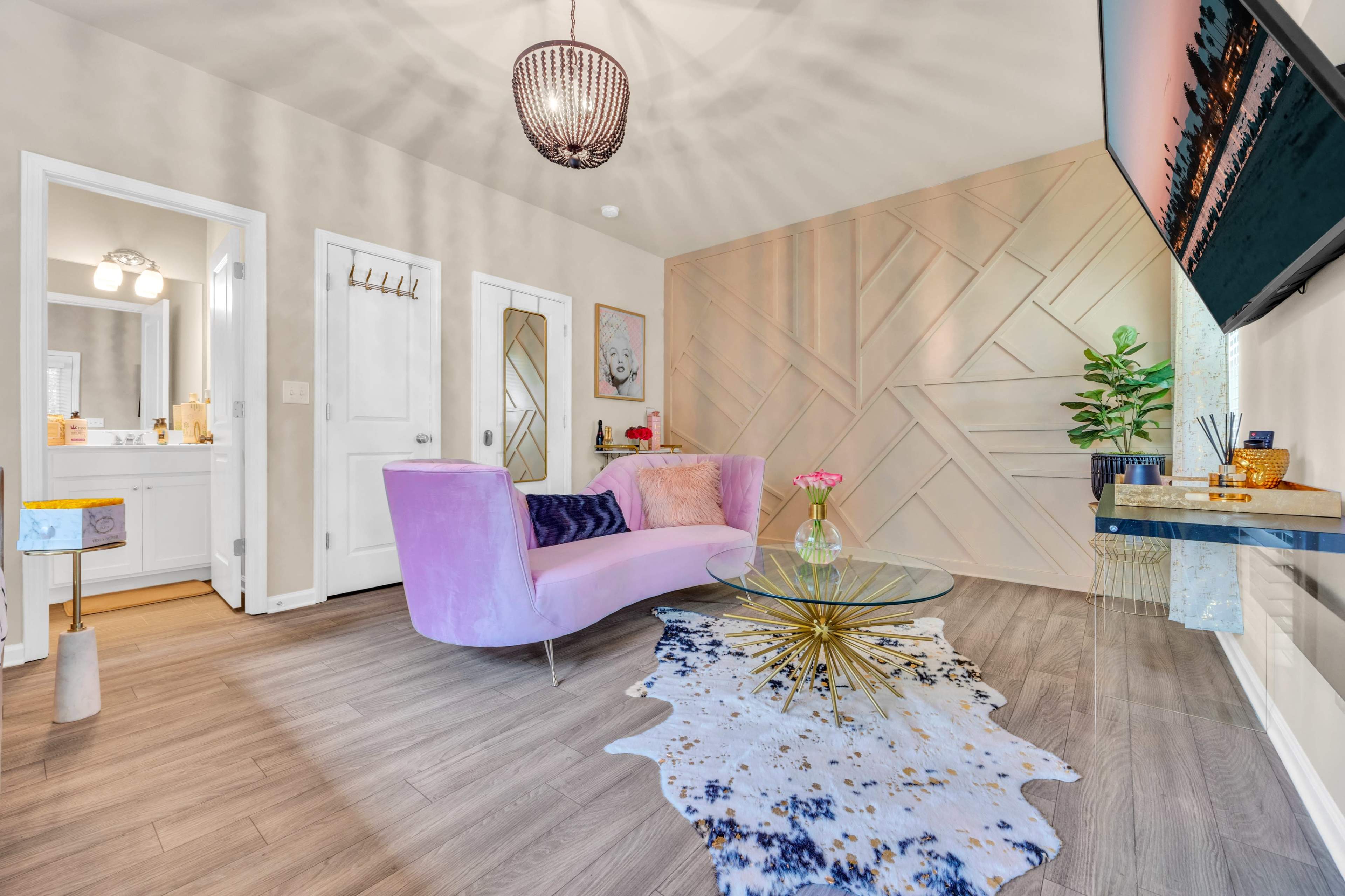 A modern living room features a pink couch, a round glass coffee table on a patterned rug, and a decorative wall with geometric designs.