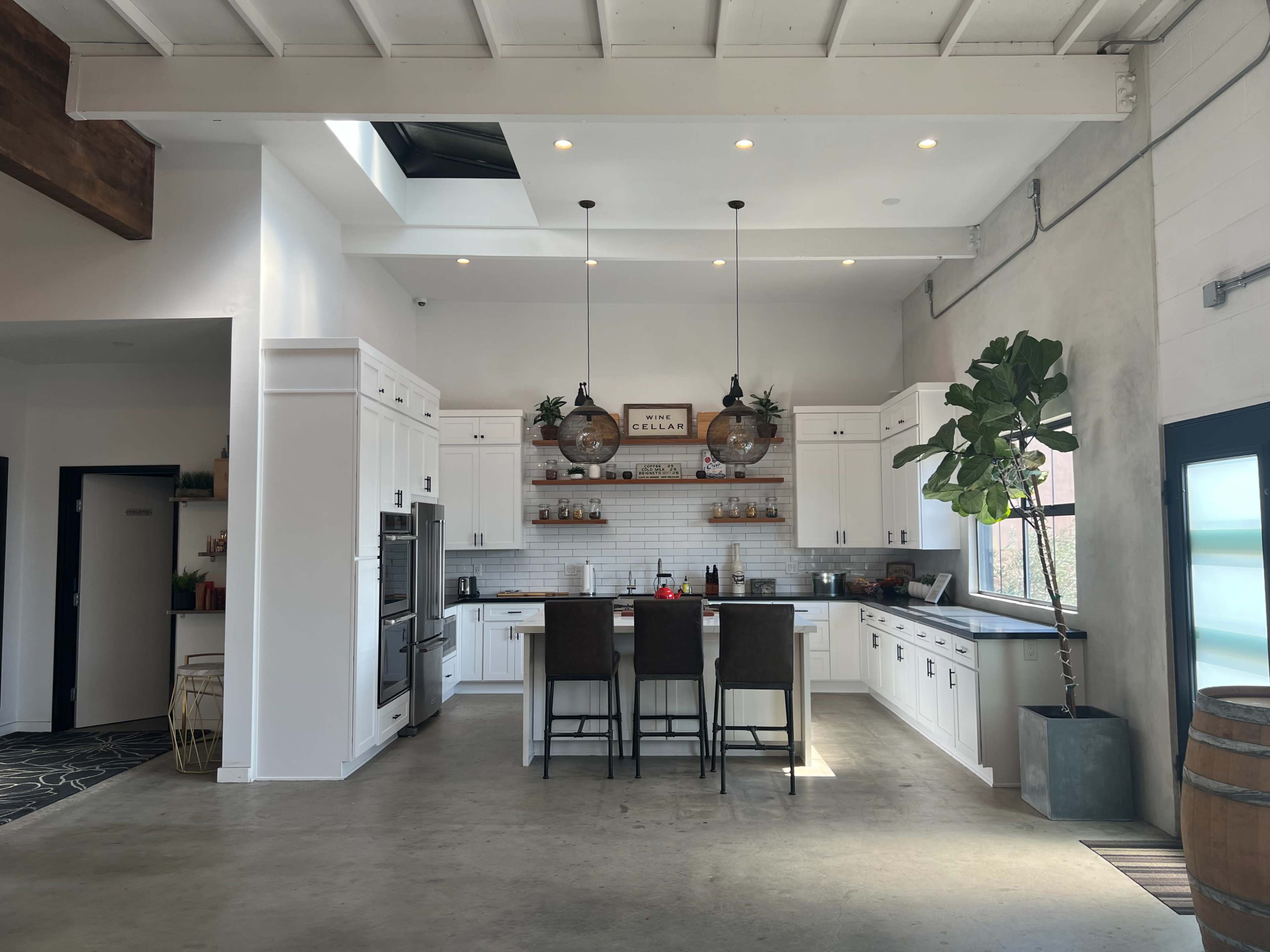 A modern kitchen with white cabinetry, a central island with bar stools, and large windows allowing natural light to fill the space.