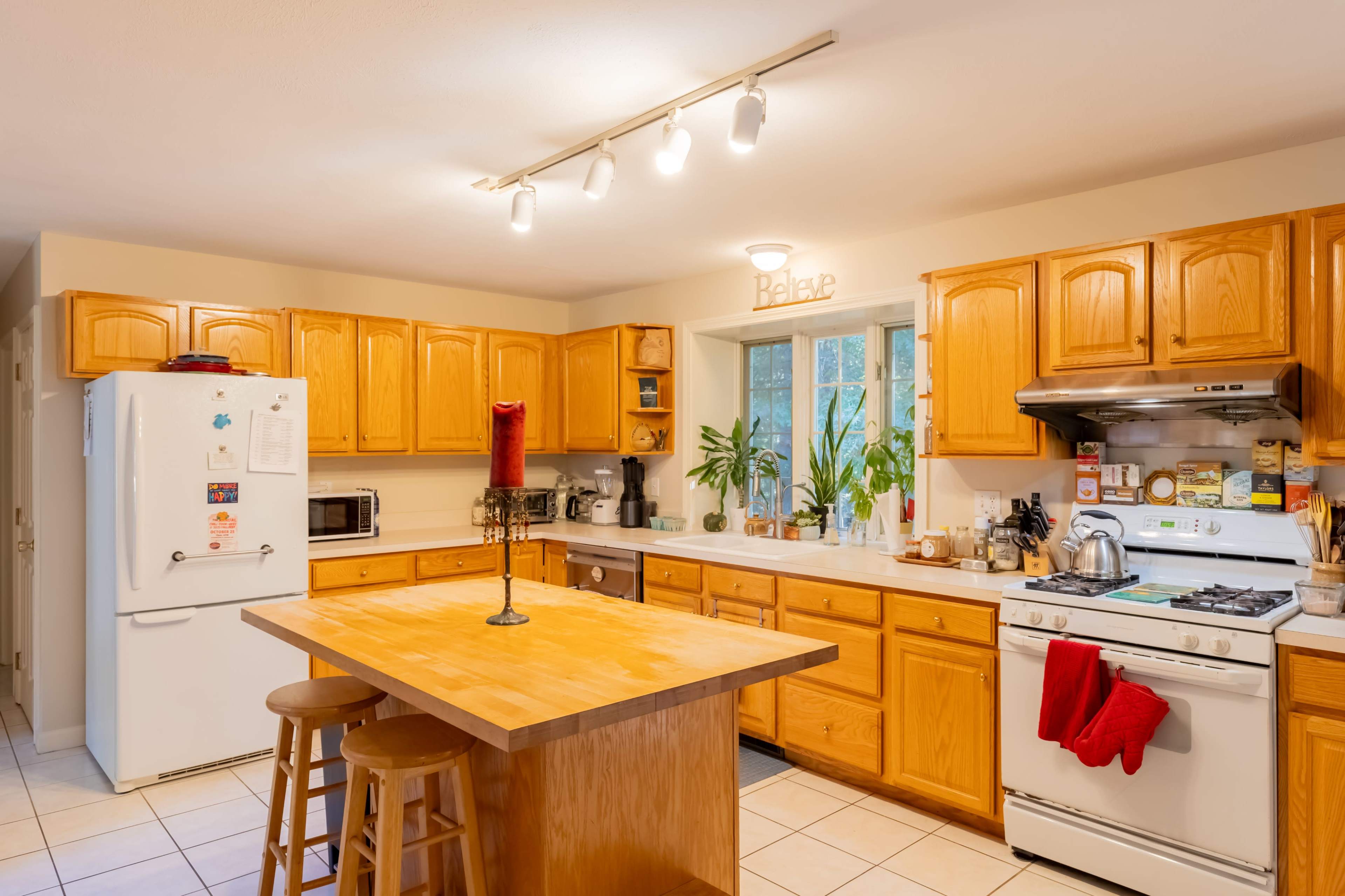 A spacious kitchen features wooden cabinets, a central island with stools, and various appliances, including a stove and refrigerator.