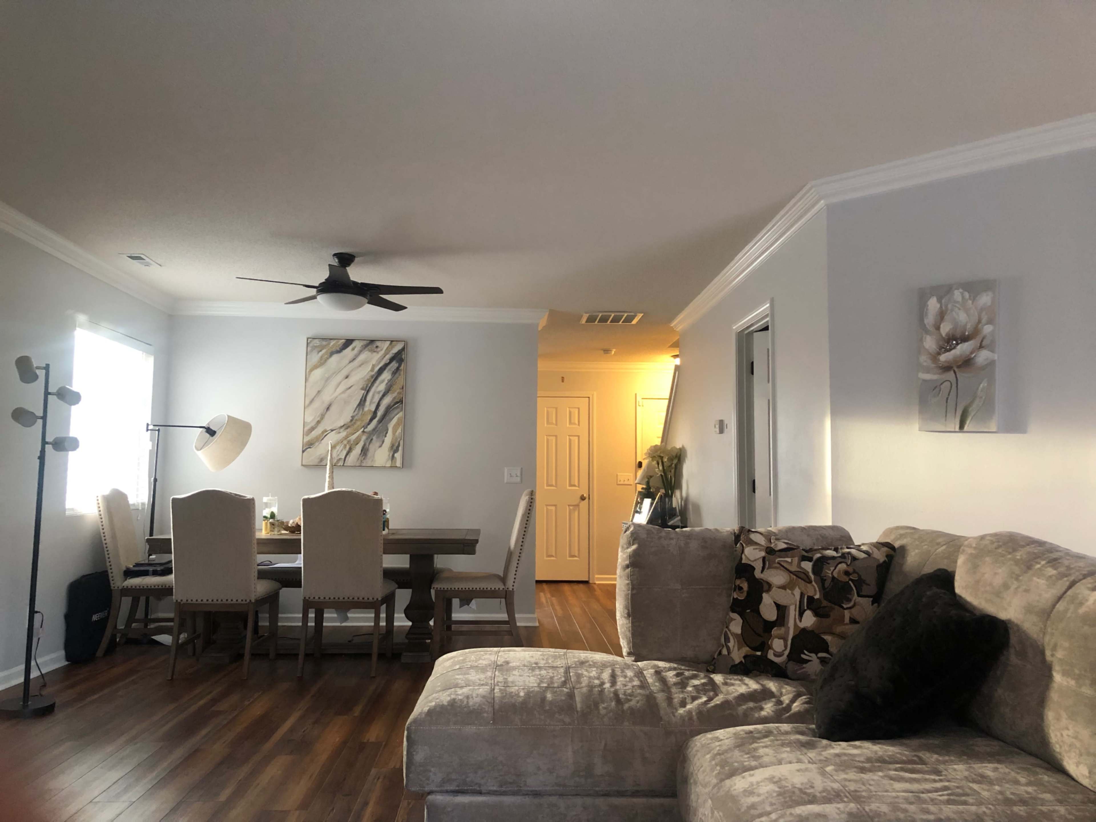 A living room with a sectional couch, a dining area with a table and chairs, and a hallway leading to a door.