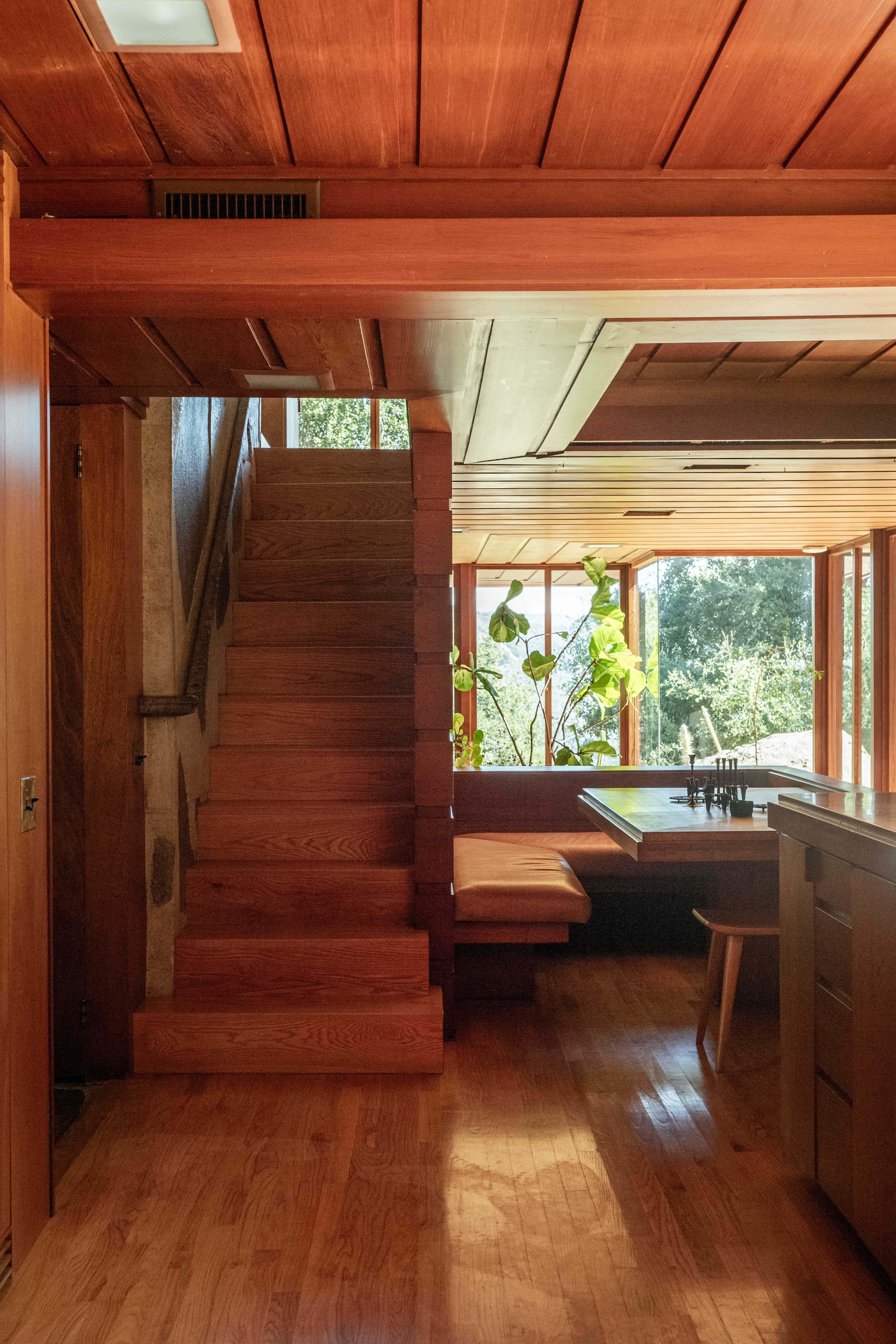 A wooden interior space featuring a staircase leading to an upper level, with a dining area and large windows that allow natural light to enter.