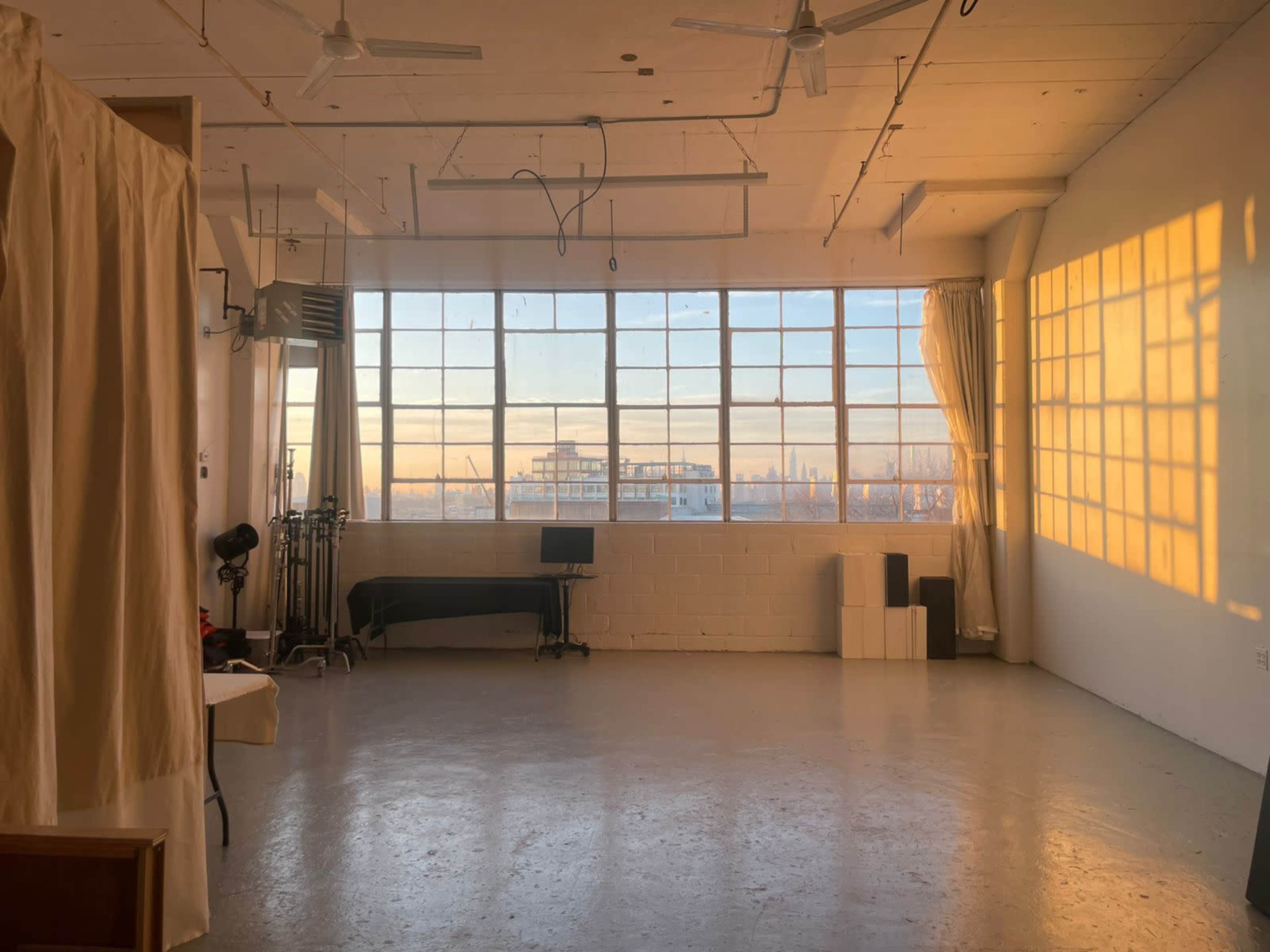 An empty studio space with large windows casting shadows on the floor and walls as sunlight enters.
