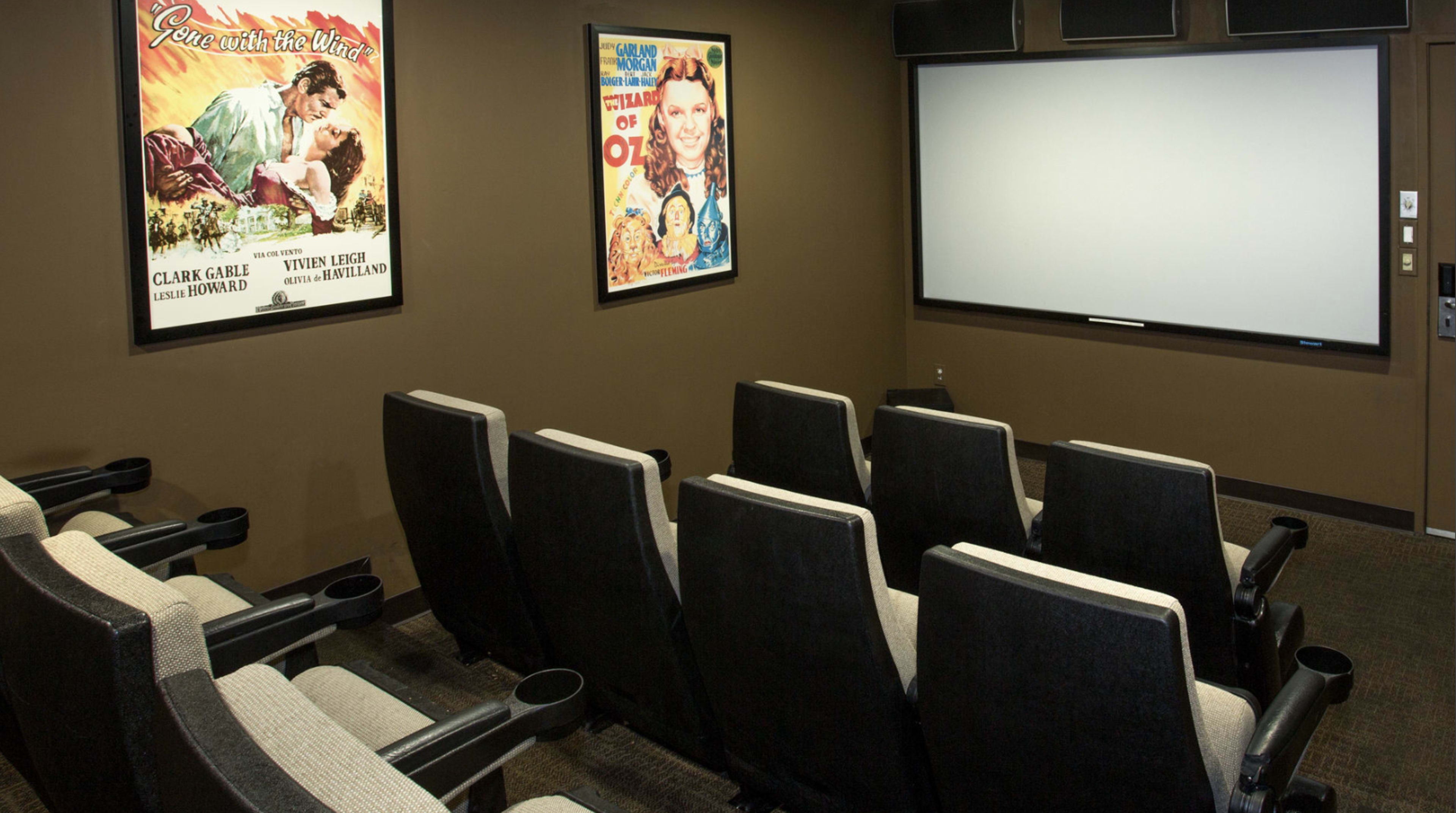 The image shows a small home theater room featuring six reclining chairs, a blank projection screen, and vintage movie posters on the walls.