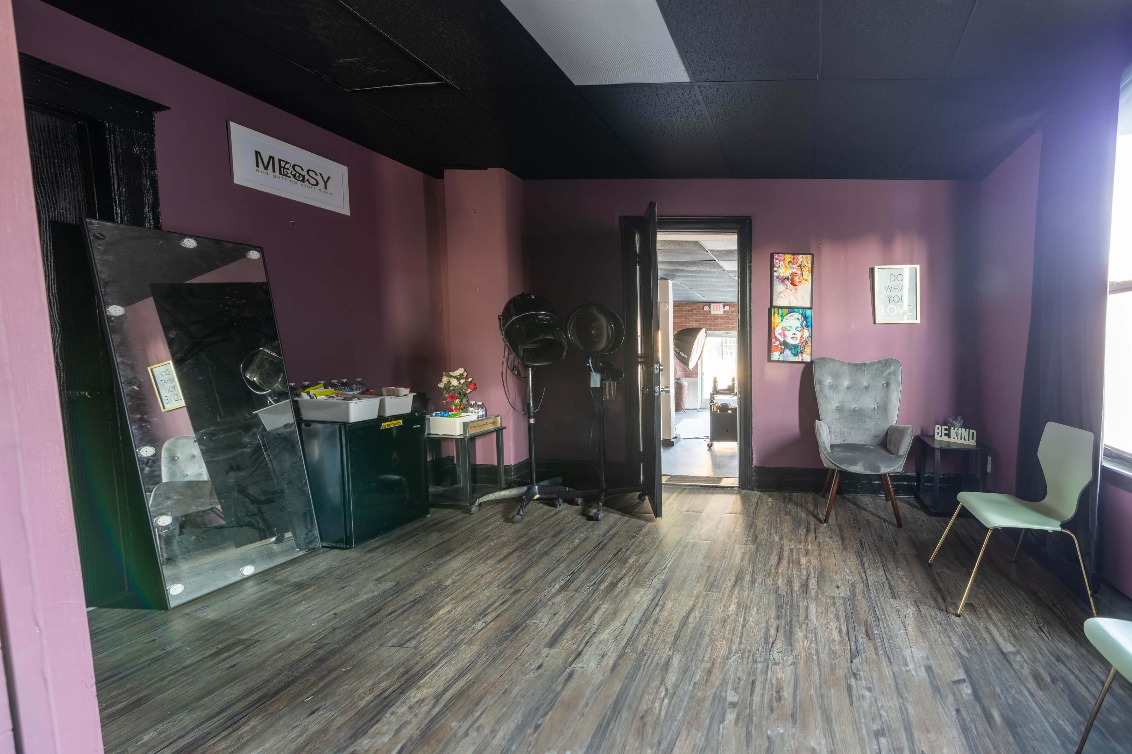 A room with purple walls, a mirror, a couple of chairs, and a doorway leading to another space.