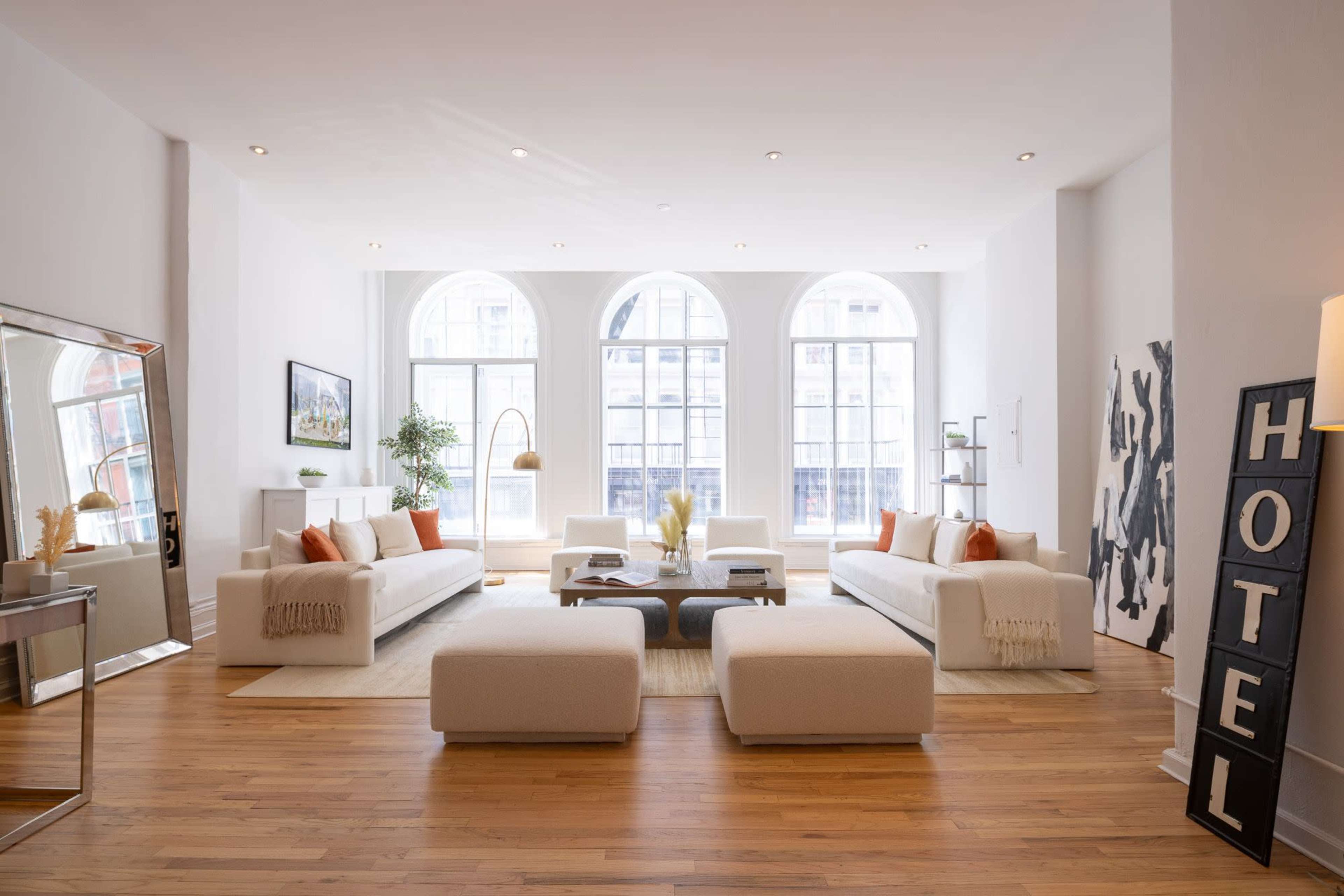 A spacious living room with large arched windows, two white sofas, a coffee table, and decorative elements including plants and artwork.