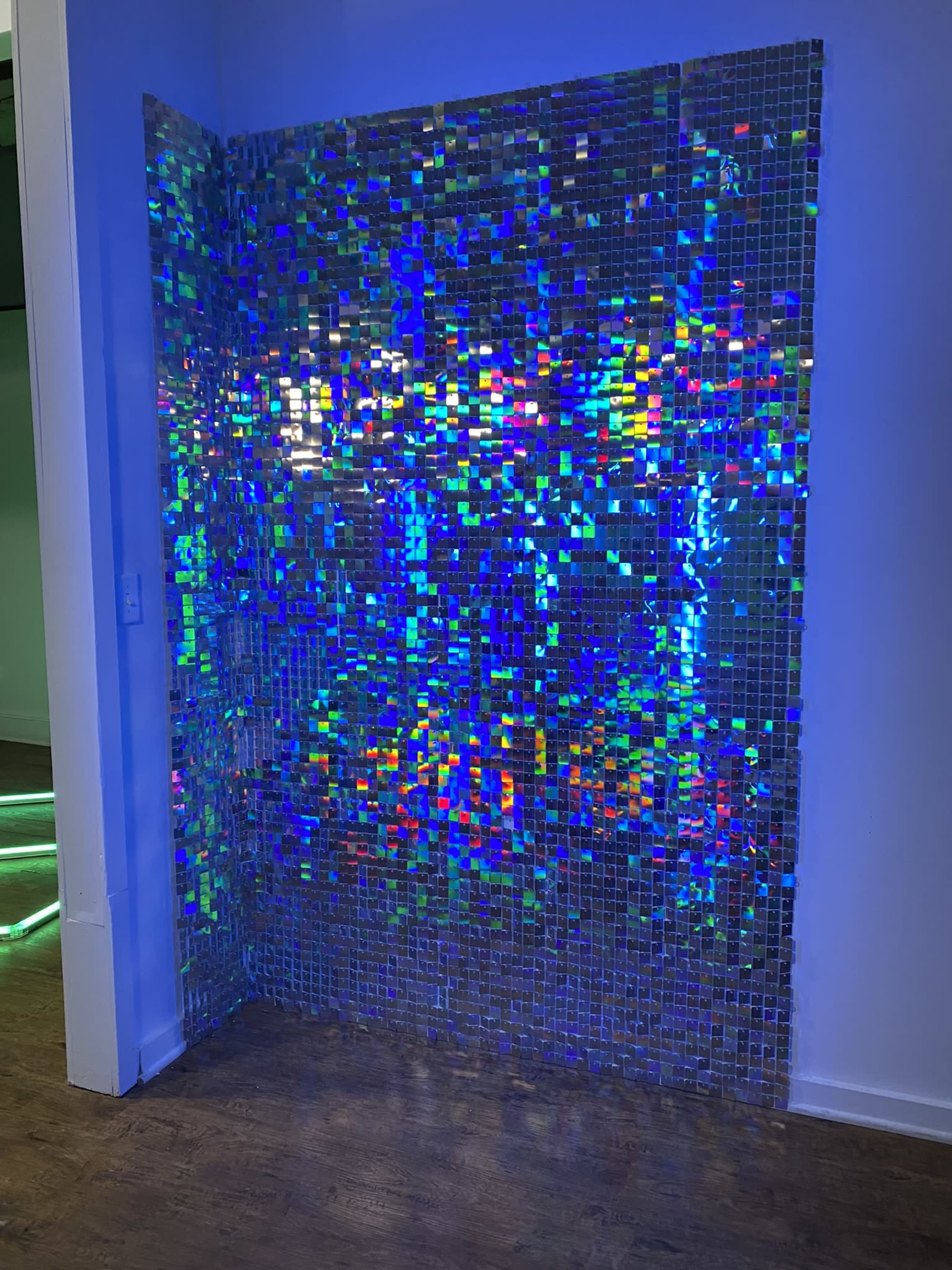 A wall covered with shimmering, reflective squares that create a colorful pattern under blue lighting.