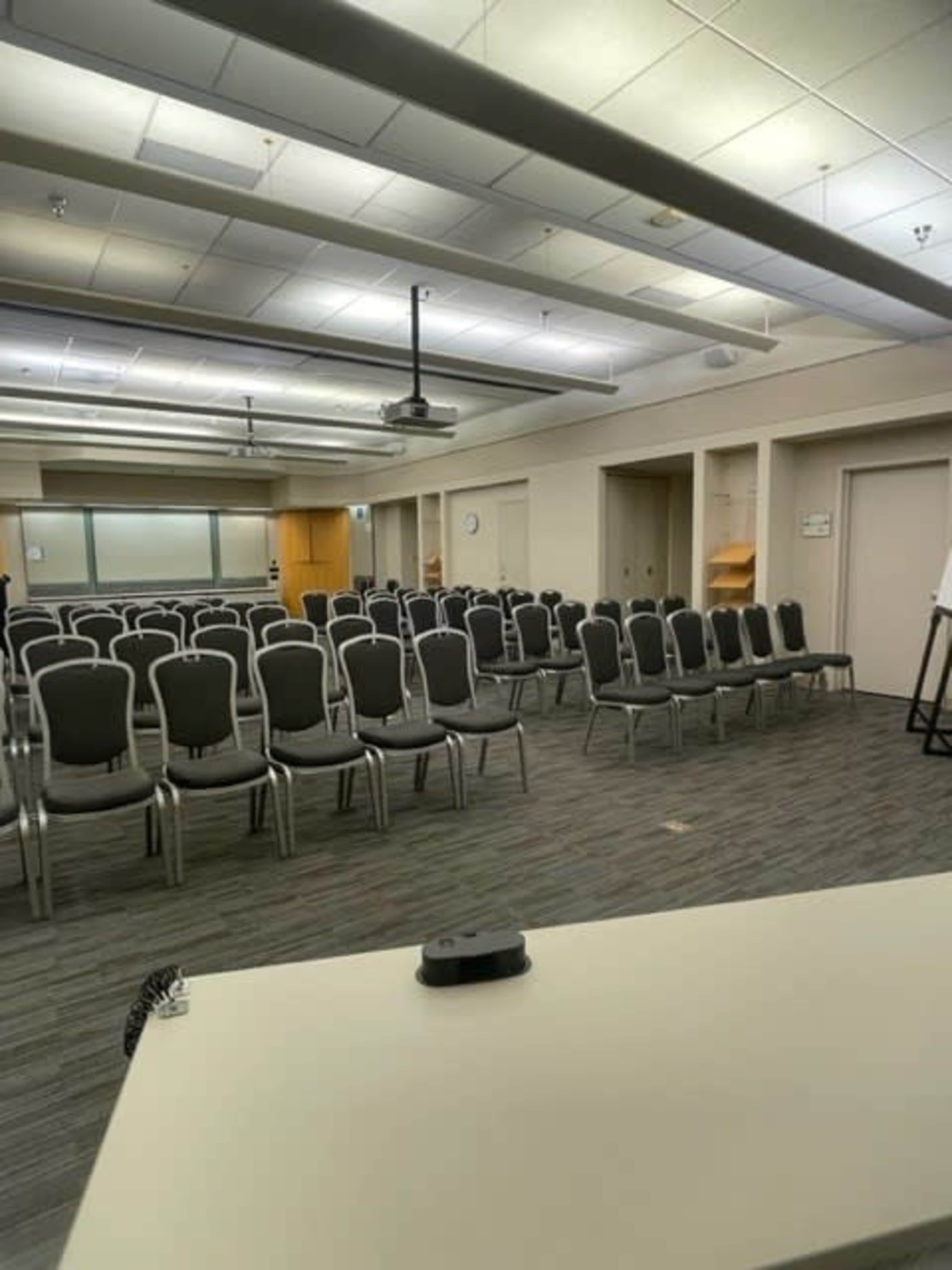 A conference room is set up with rows of empty chairs facing a presentation area at the front.