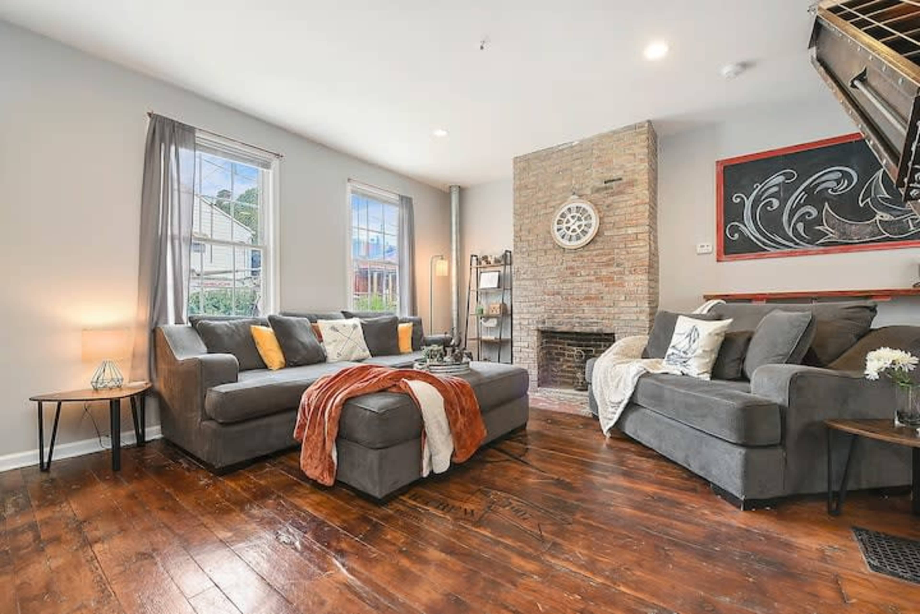 The living room features a gray sectional sofa, a matching loveseat, a brick fireplace, and large windows allowing natural light to enter the space.