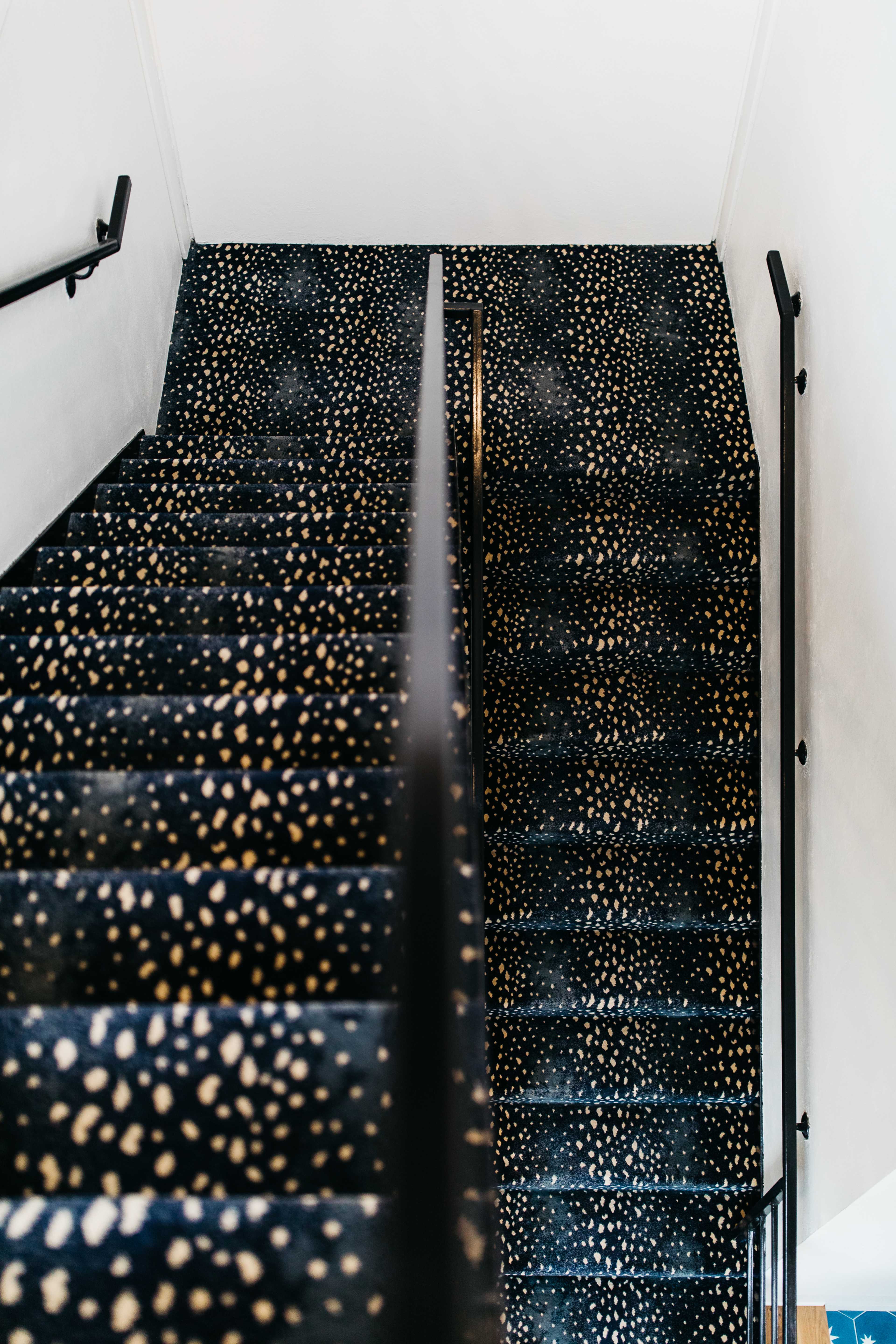 The image shows a staircase with a dark carpet featuring a pattern of light-colored dots, flanked by black railings.
