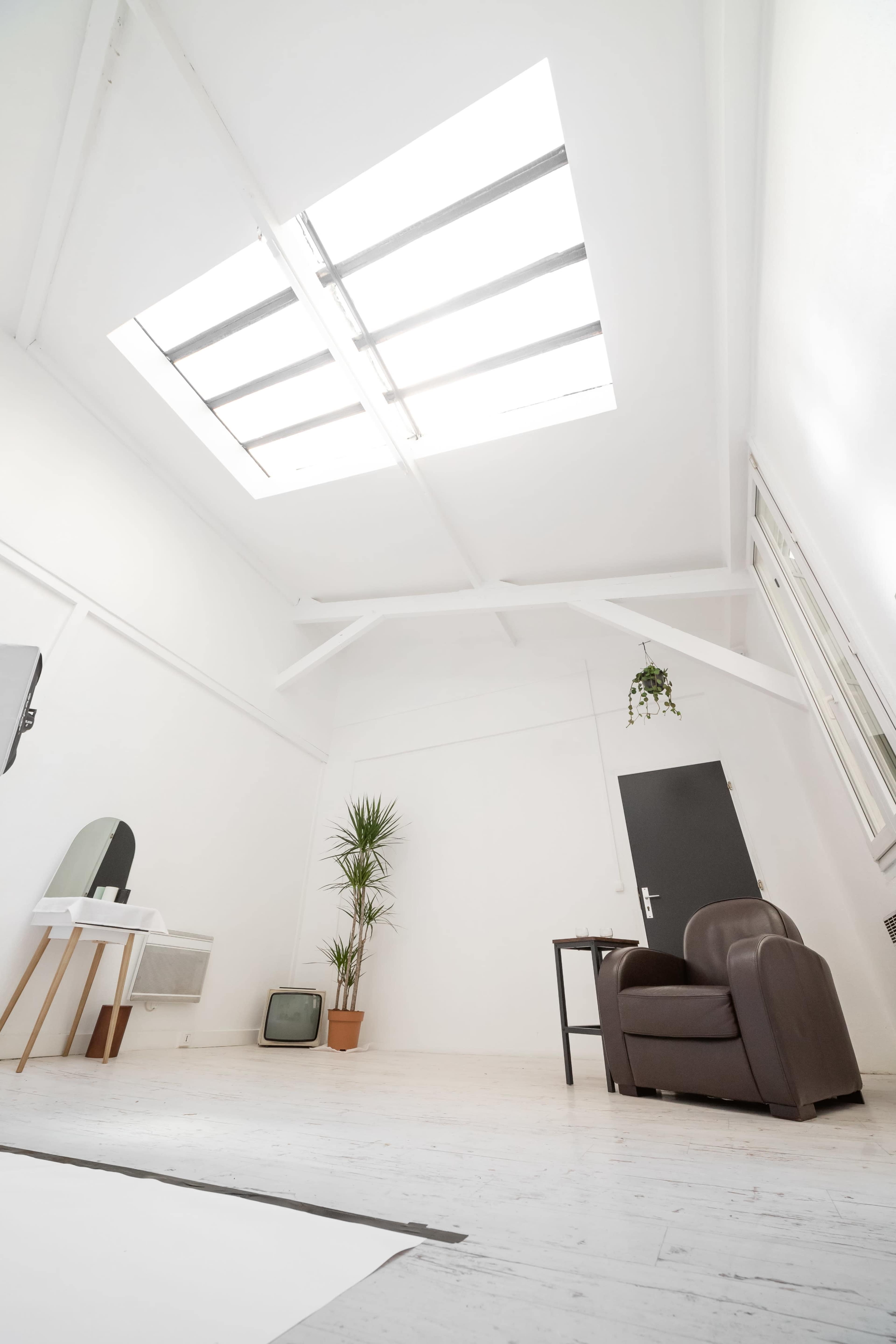 A spacious, minimalist room with a skylight, a brown leather armchair, a small table, a potted plant, and an old television set.