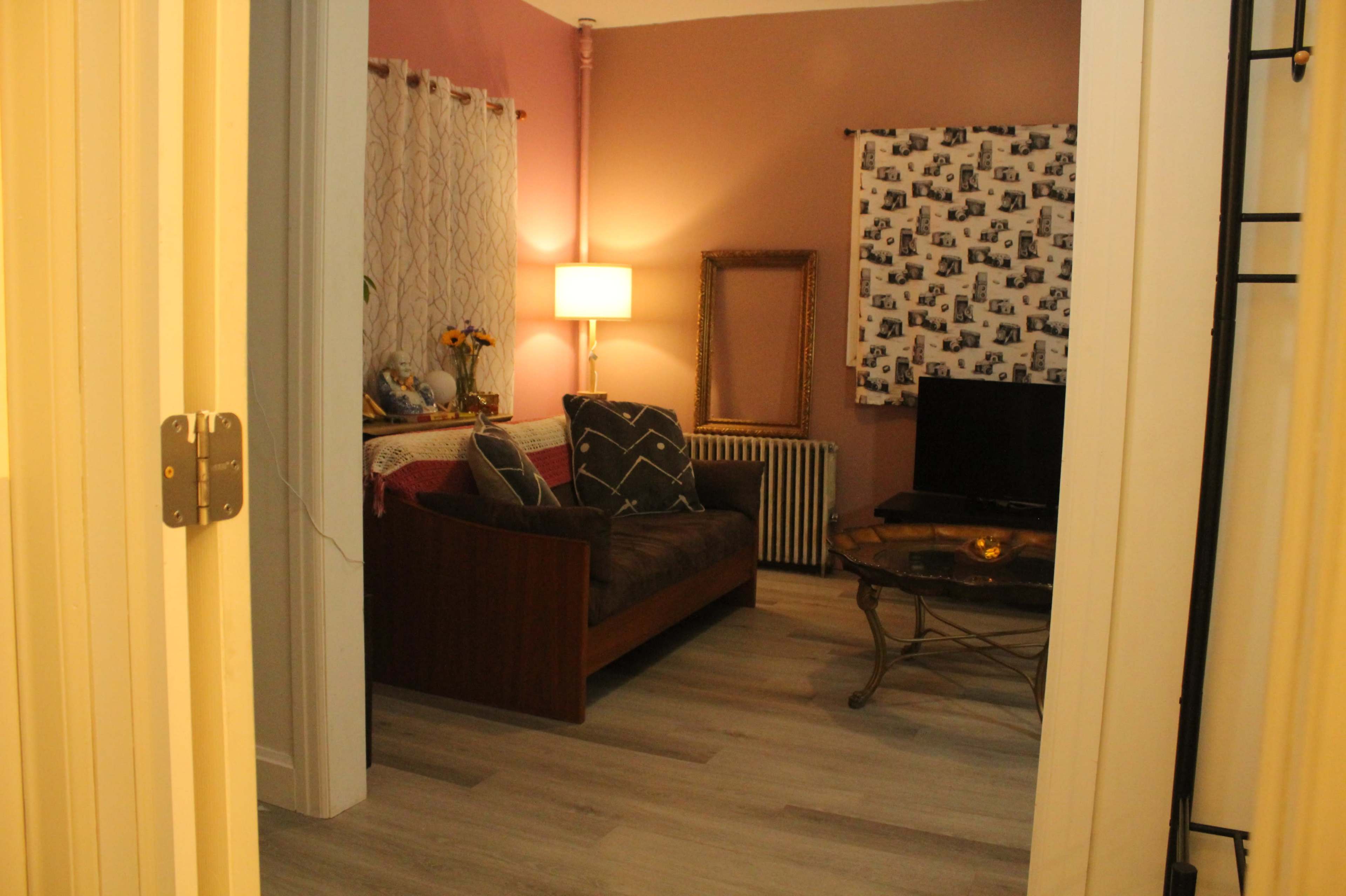 The image shows a cozy living room with a brown couch, a coffee table, a TV, and decorative curtains.