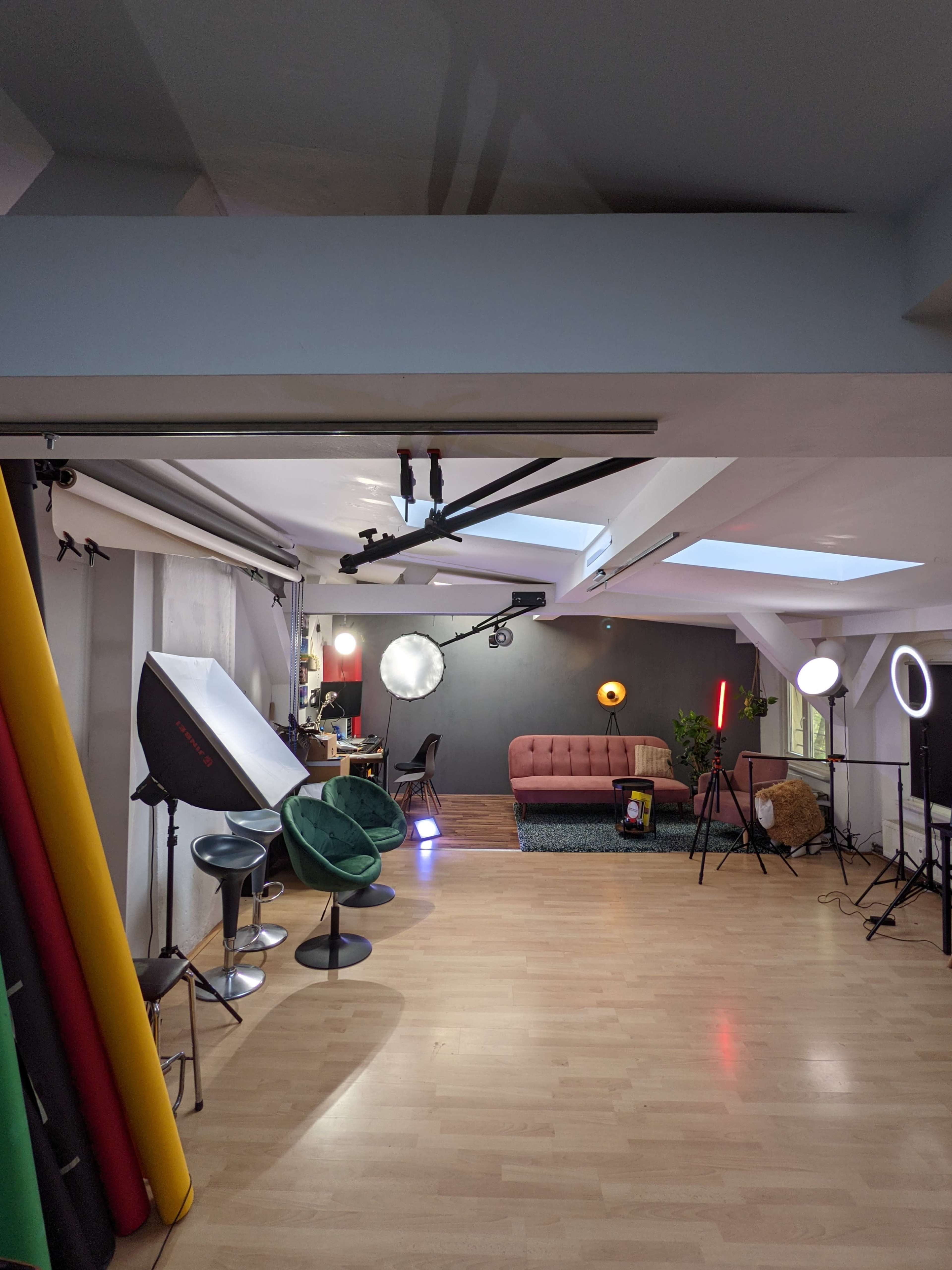 A photography studio with various lighting equipment, a red sofa, and colorful backdrop rolls on one side.