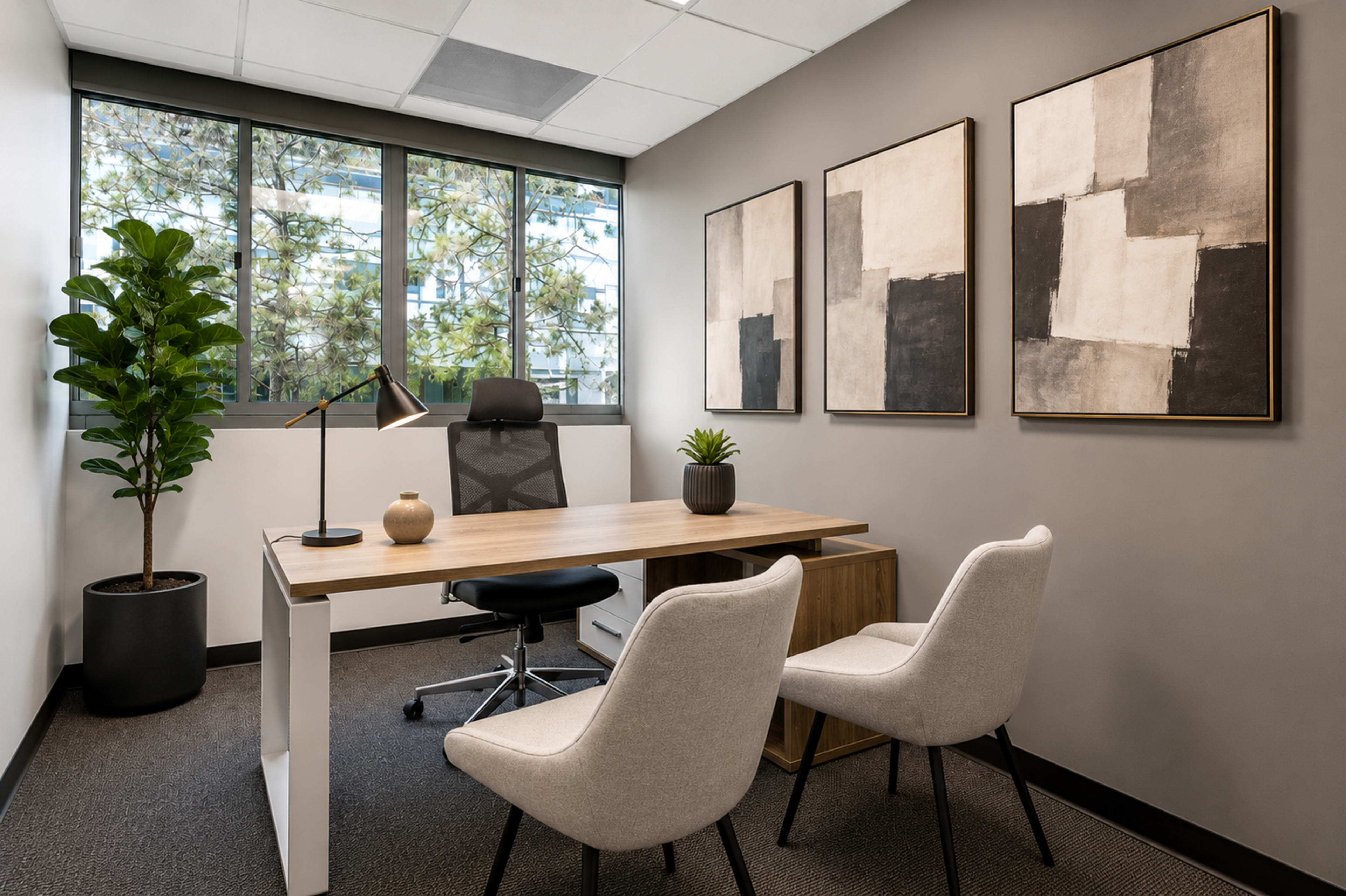 A modern office space features a wooden desk with a chair, two additional chairs, indoor plants, and abstract wall art.